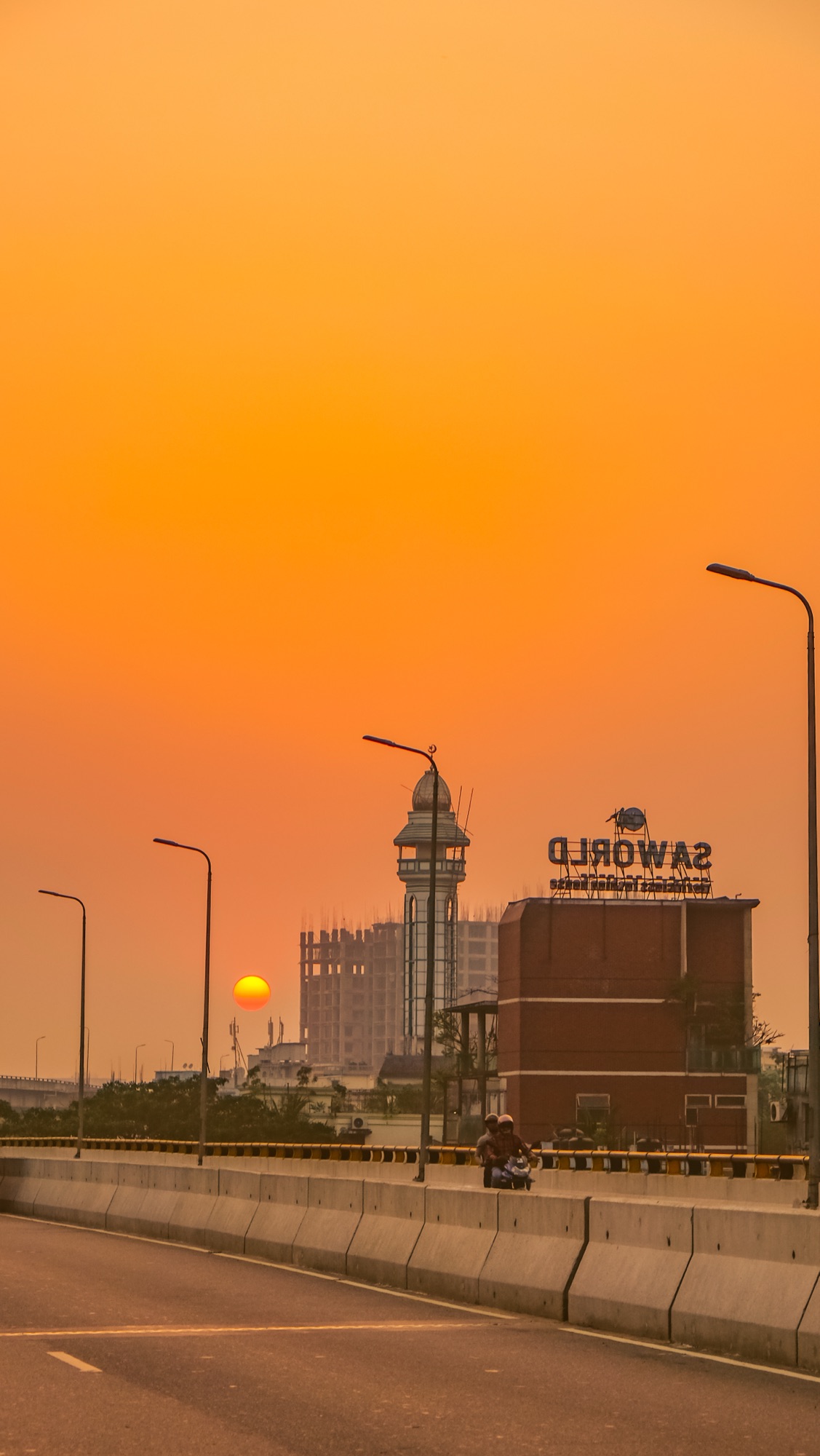 A blazing orange sunset over a lakeside town with mountains behind, Bangladesh