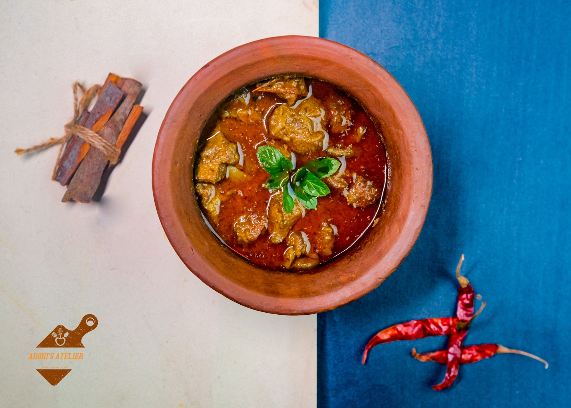Clay pot of slow-cooked curry garnished with mint on a dark blue background with chilies
