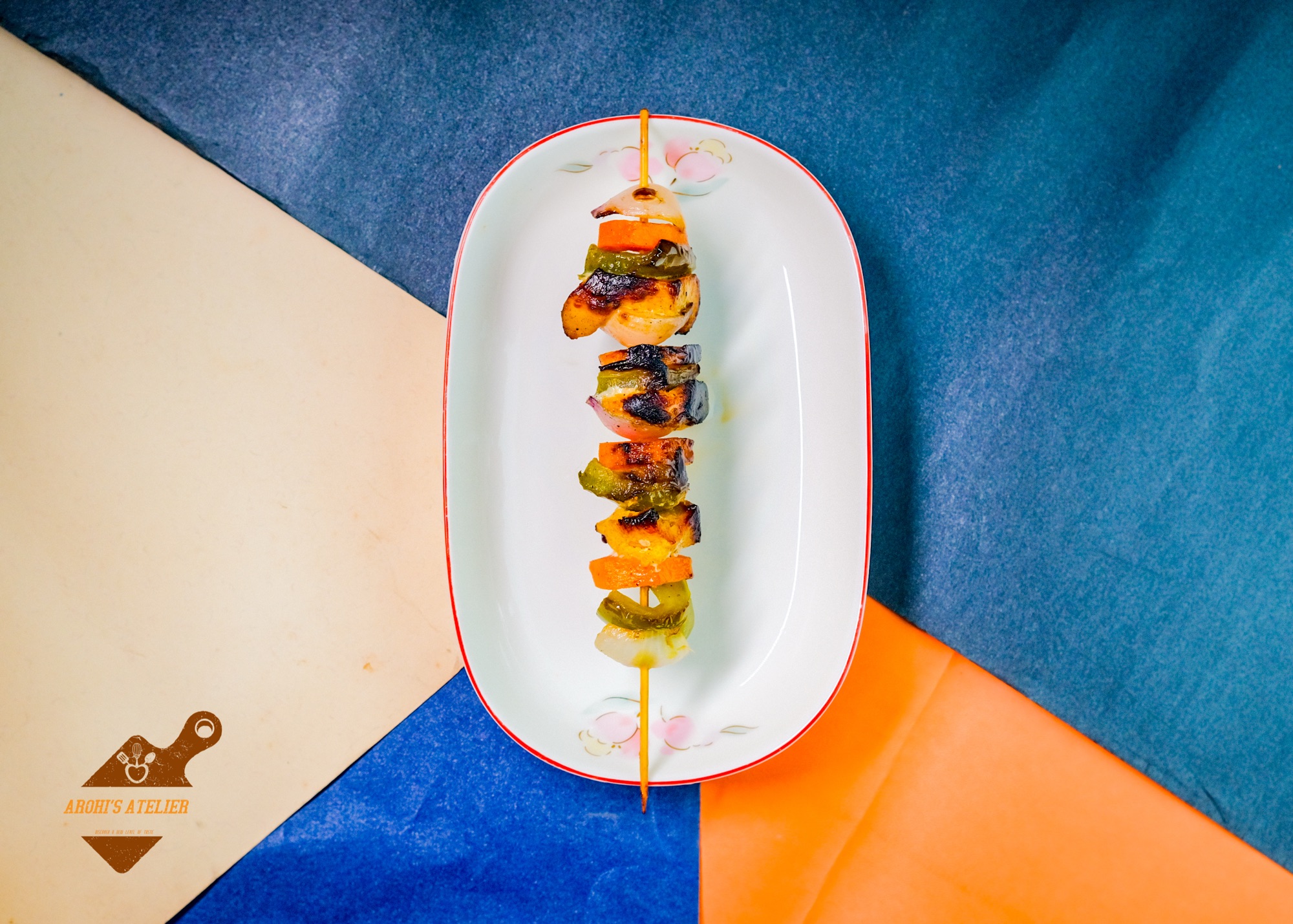 Skewered grilled kebabs plated on white against a bold orange and blue background