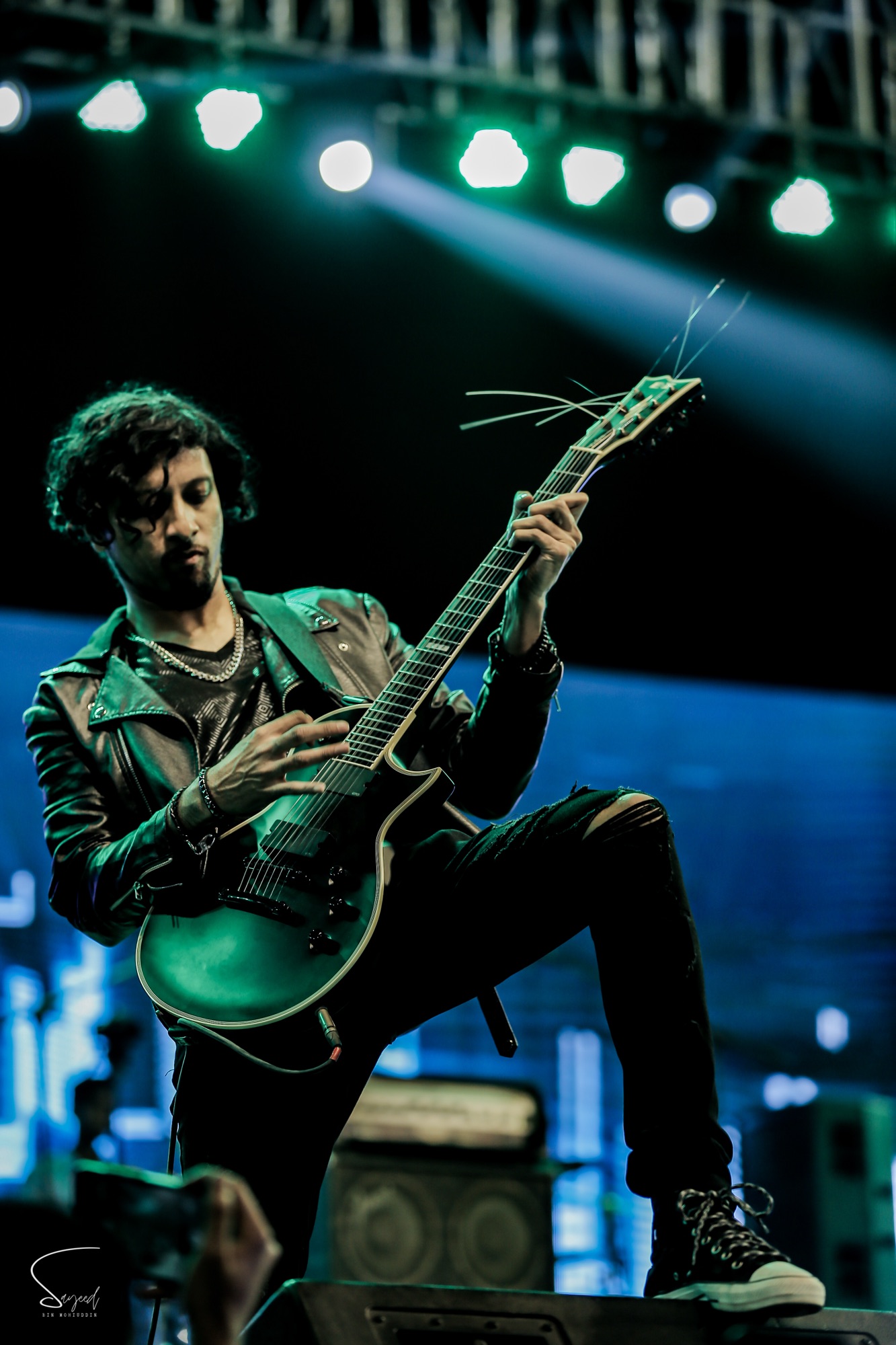 Shishir Ahmed from Aurthohin shredding with one leg up on the monitor under green stage light in Dhaka — Sayeed BM