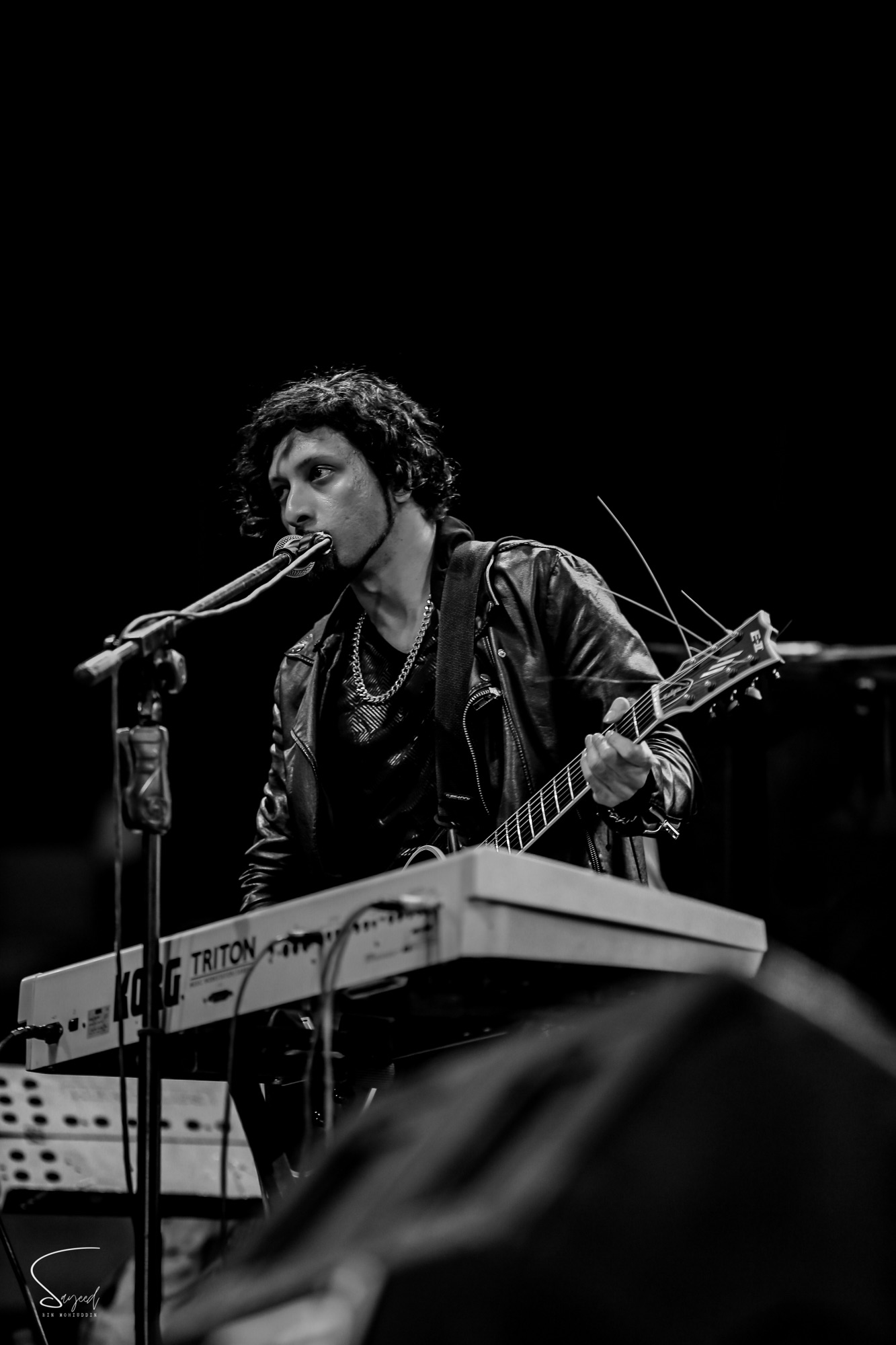 Musician playing harmonica into the mic while gripping a guitar neck, black-and-white concert photo from Dhaka — Sayeed BM