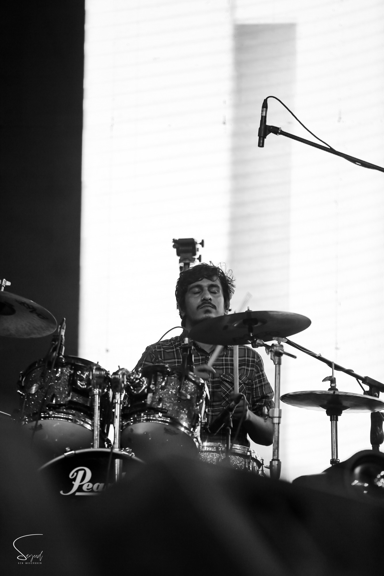 Drummer caught mid-beat against a bright backlit screen, black-and-white concert photo from Dhaka — Sayeed BM