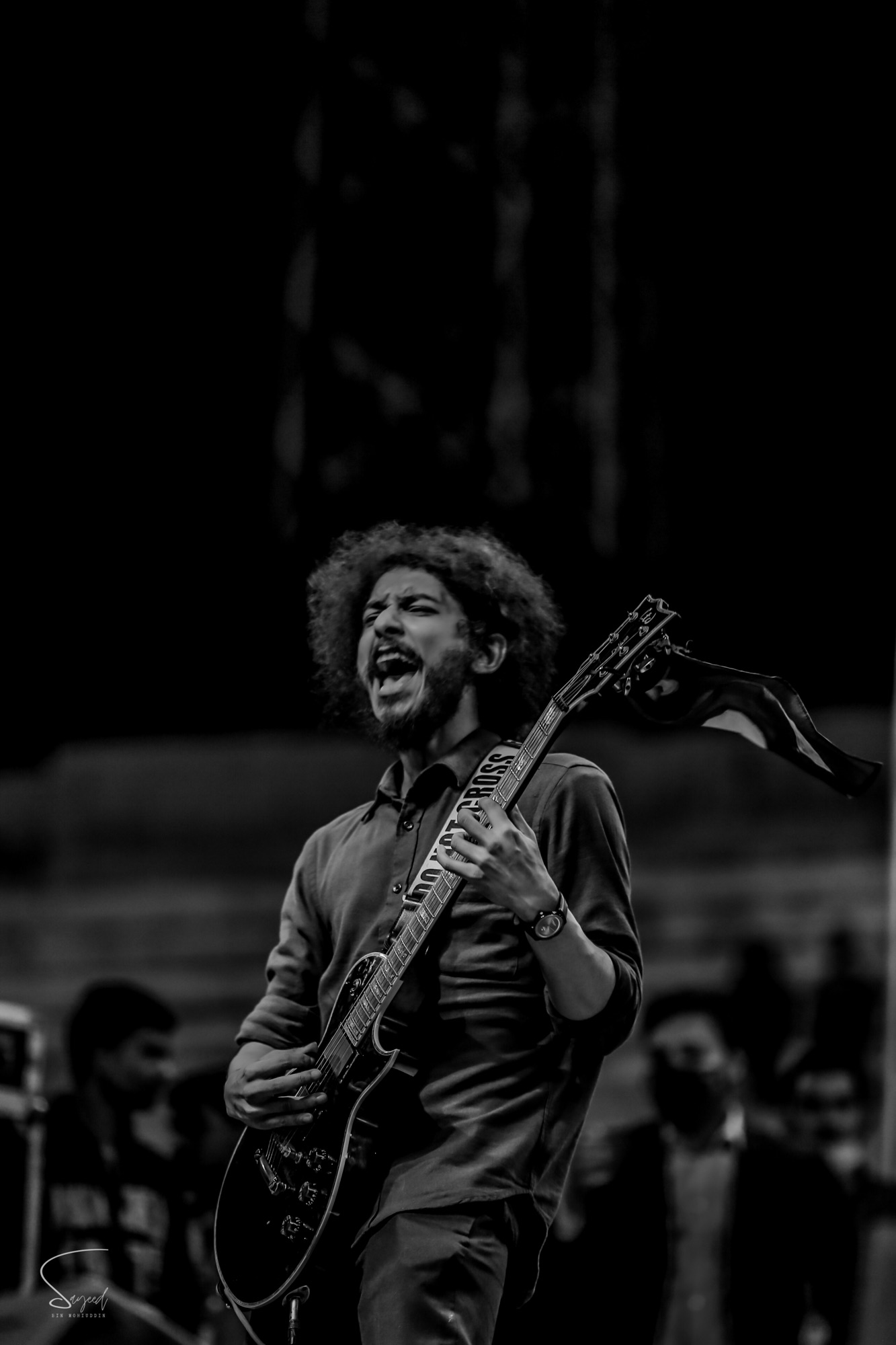Curly-haired guitarist mid-scream with guitar raised, black-and-white shot at a concert in Dhaka — Sayeed BM