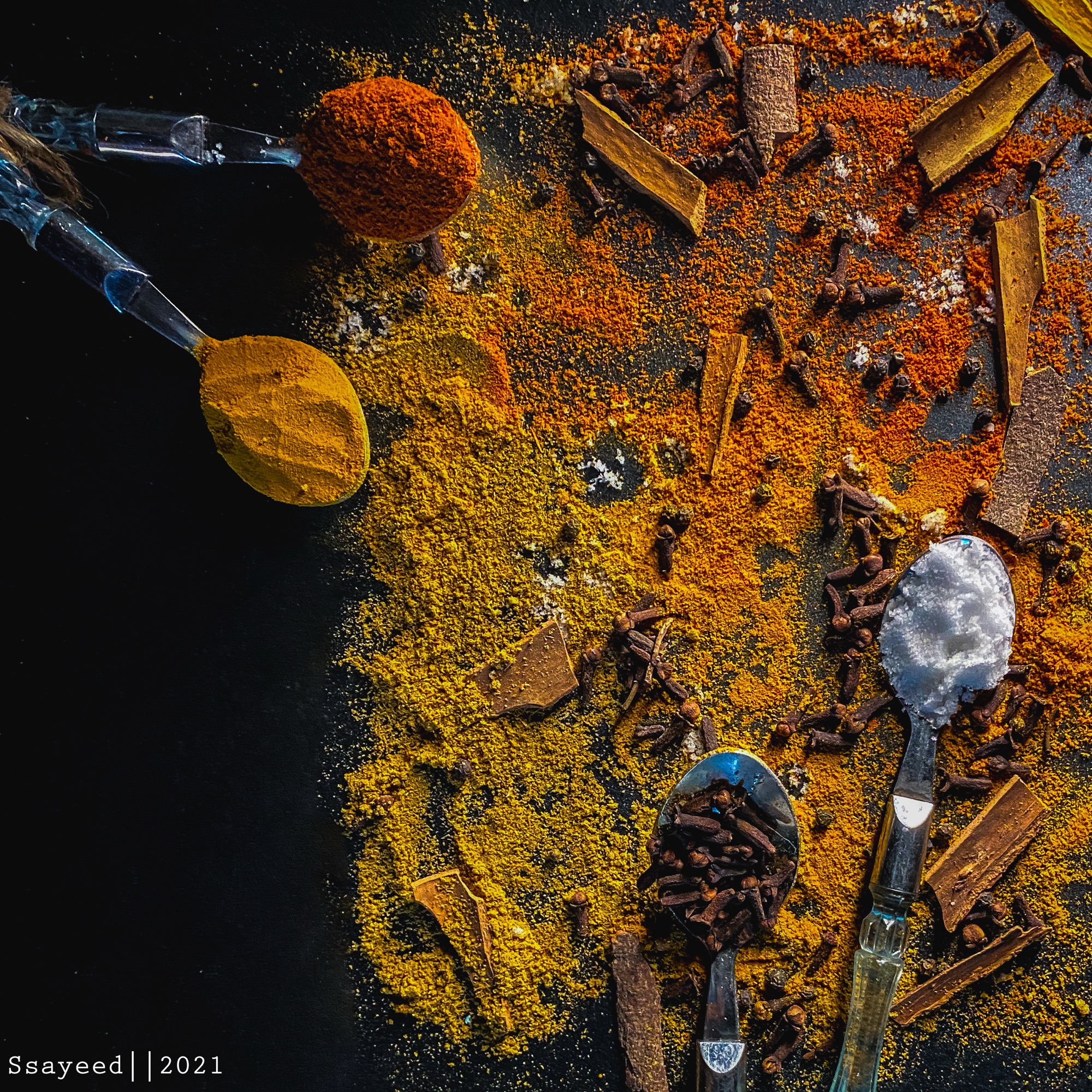 Overhead flat lay of turmeric powder, whole spices and a wooden spoon