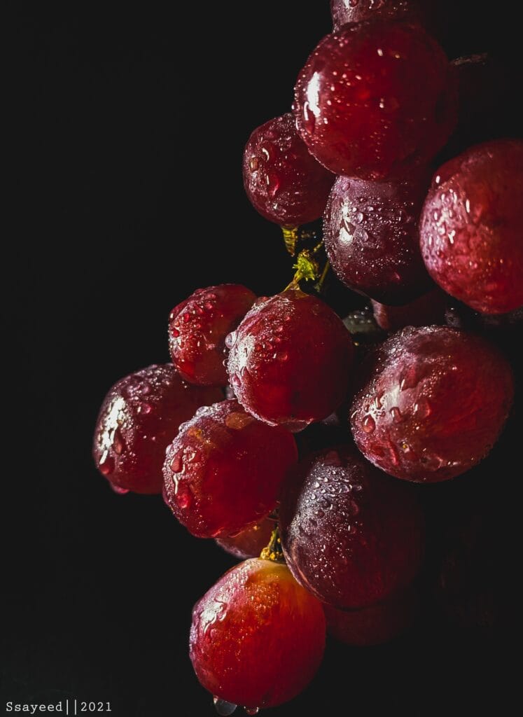 A photograph of Grapes with water bubbles in a dark background and lighting
