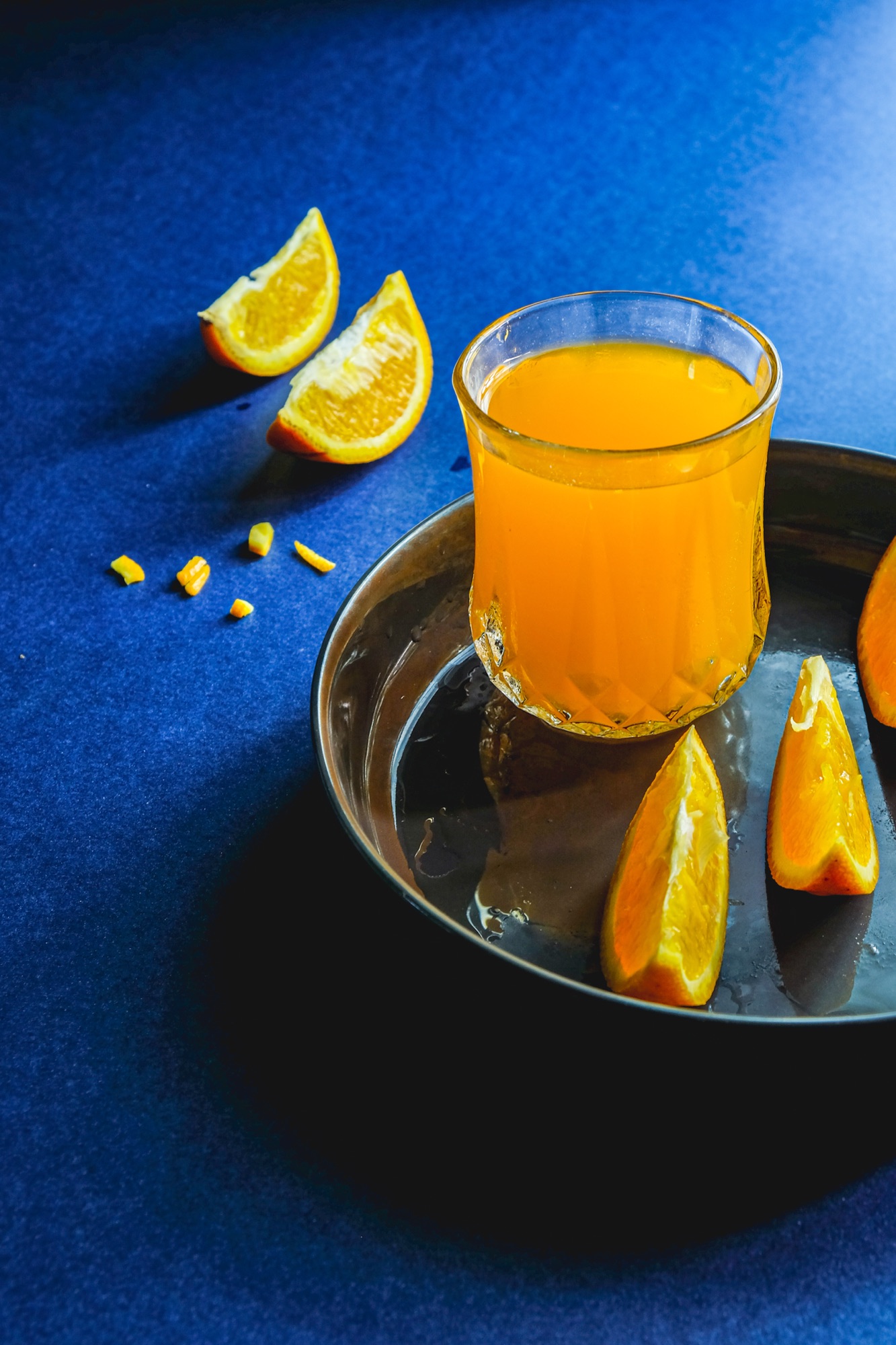 Glass of orange juice with orange slices on a blue textured cloth