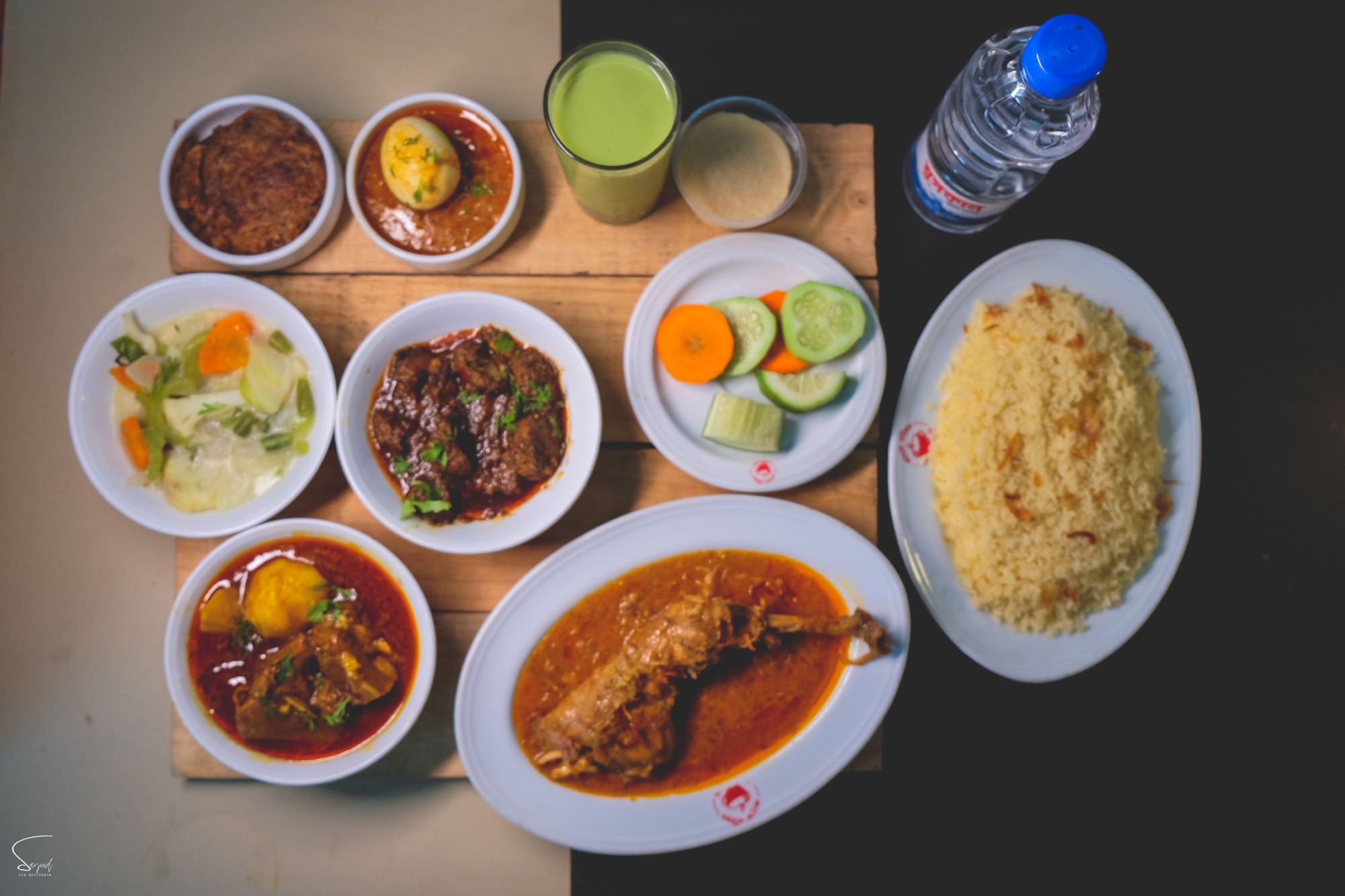 Overhead spread of Bengali curry, fried fish, rice and salad bowls on a wooden table
