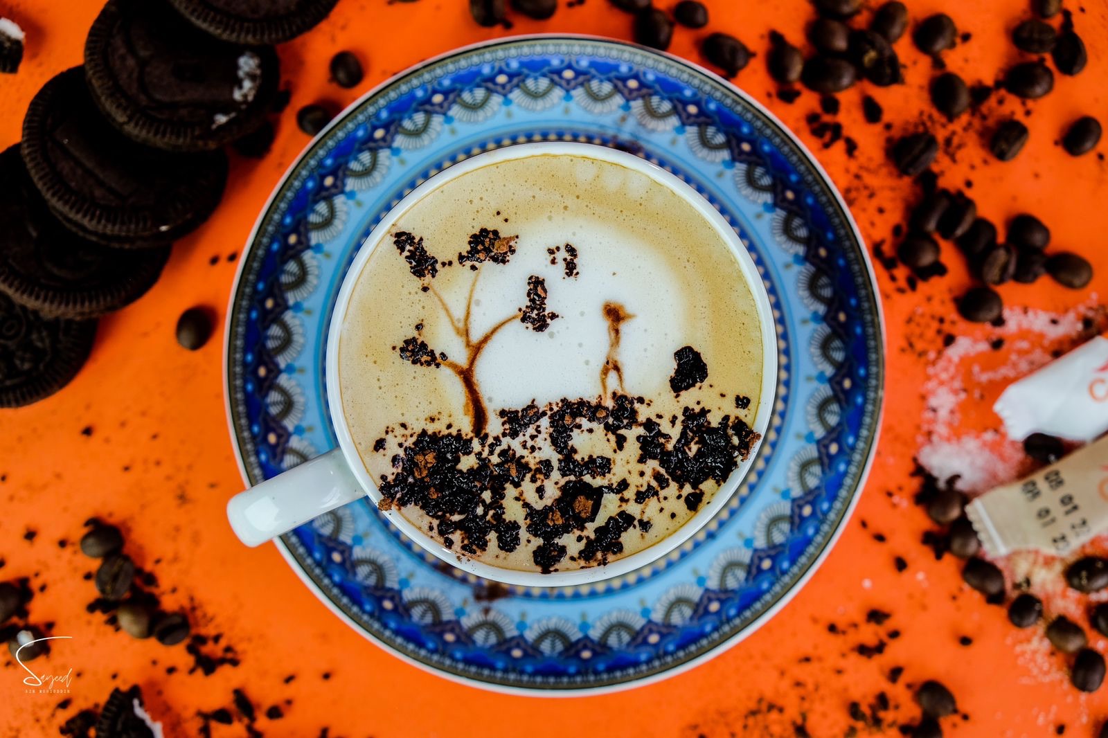 Latte with chocolate drizzle art in a blue and white cup on a bold orange background
