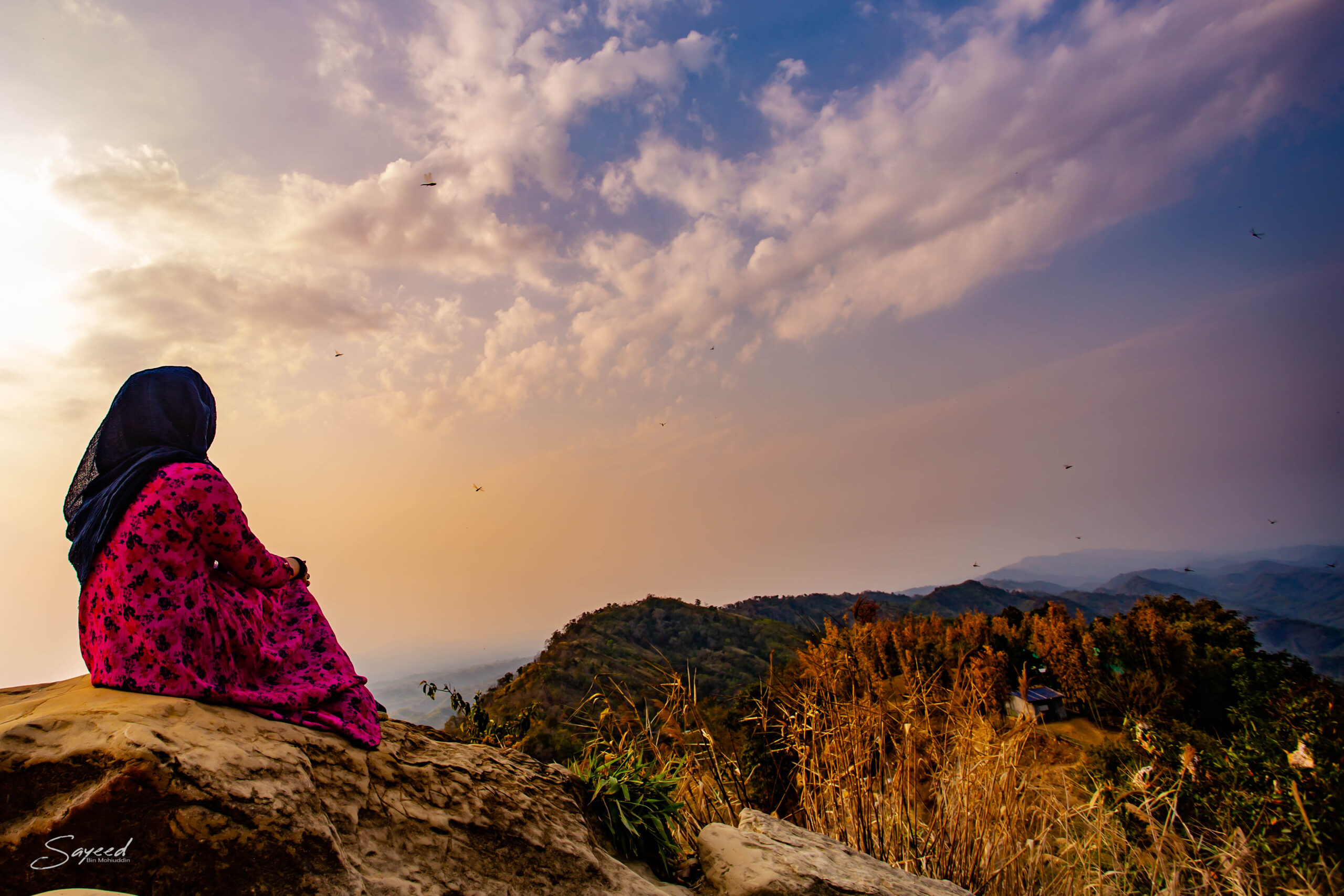 A figure sitting on a clifftop looking out over a sea of cloud at golden hour, Bandarban
