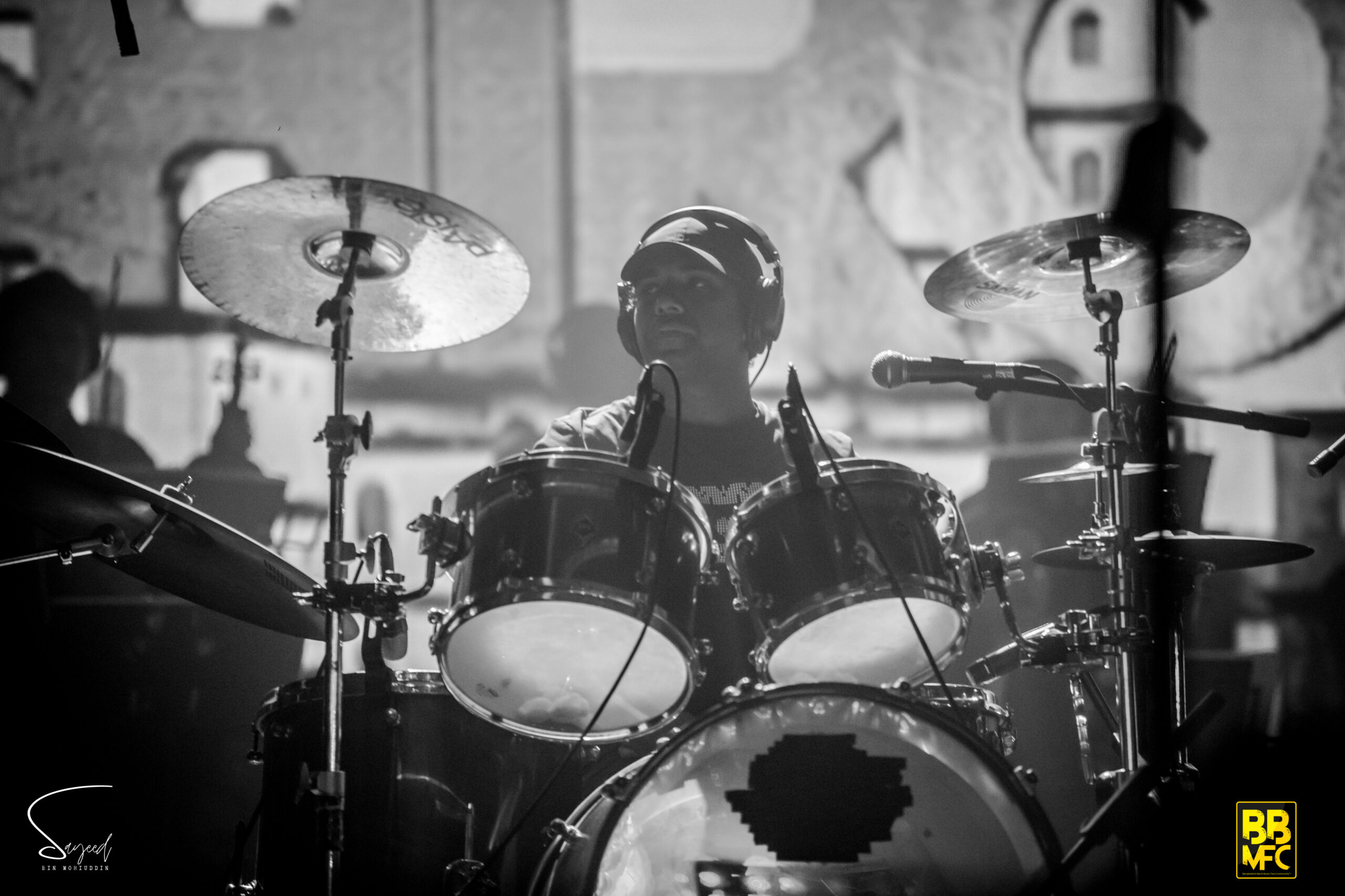 Drummer behind his kit lit by hazy stage glow, black-and-white shot from a Shironamhin concert in Dhaka — Sayeed BM