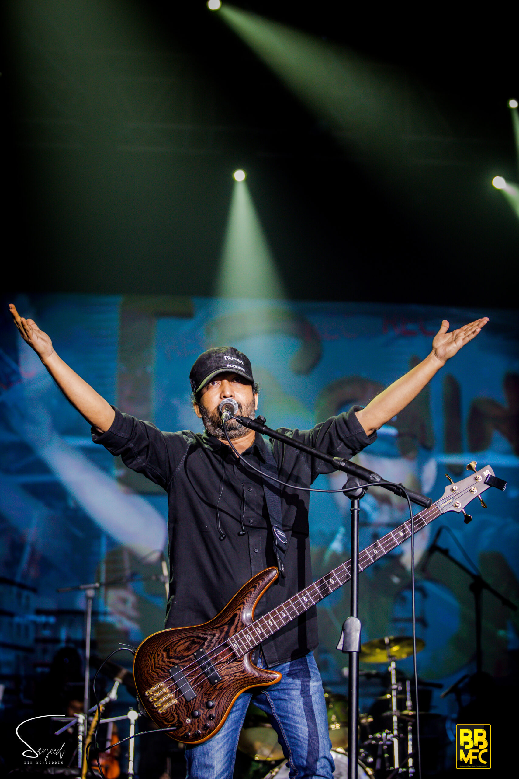 Bassist with arms outstretched mid-song, singing into the mic at a Shironamhin concert in Dhaka — Sayeed BM