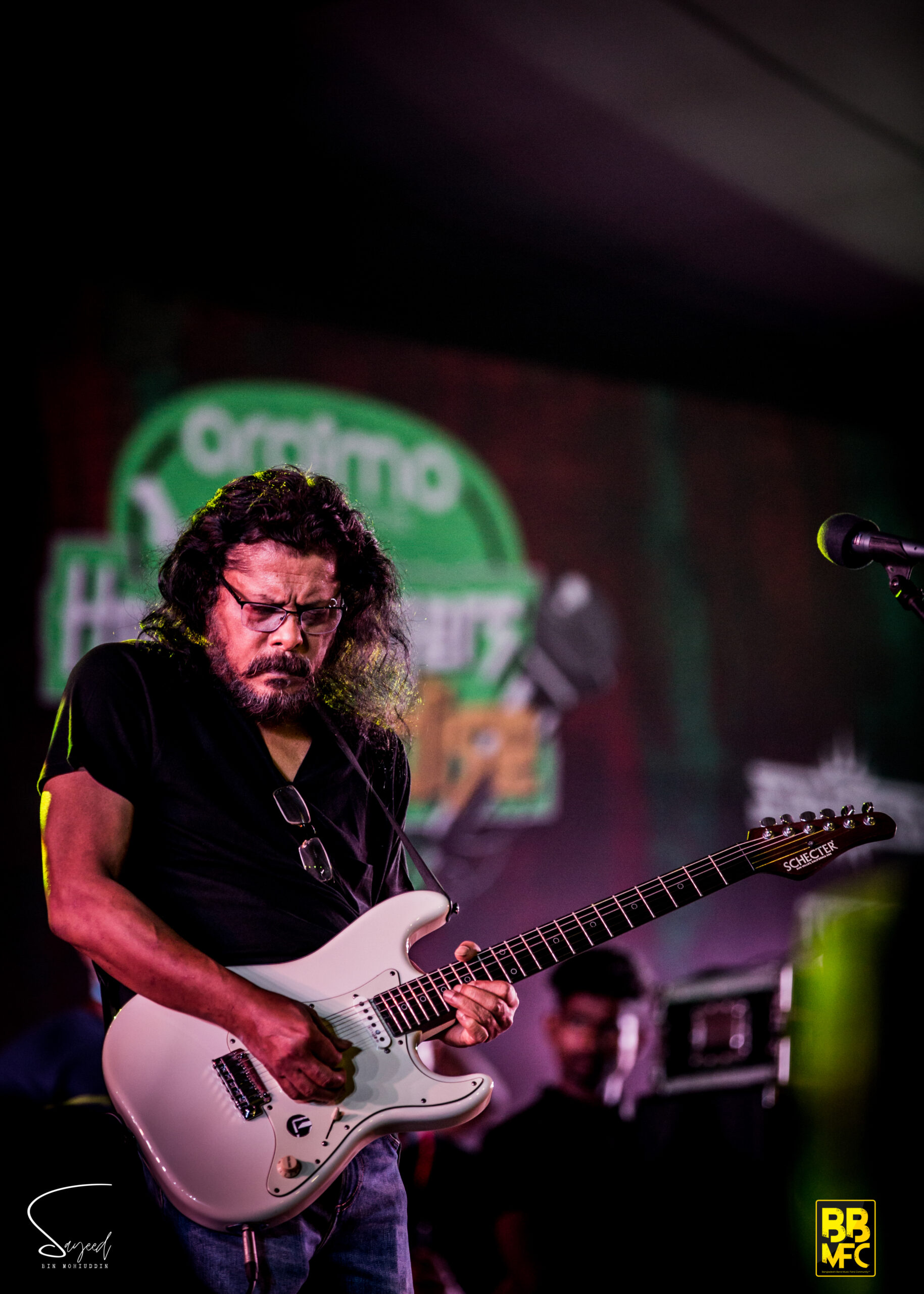 Long-haired guitarist with glasses playing a white Stratocaster under purple stage lights in Dhaka — Sayeed BM