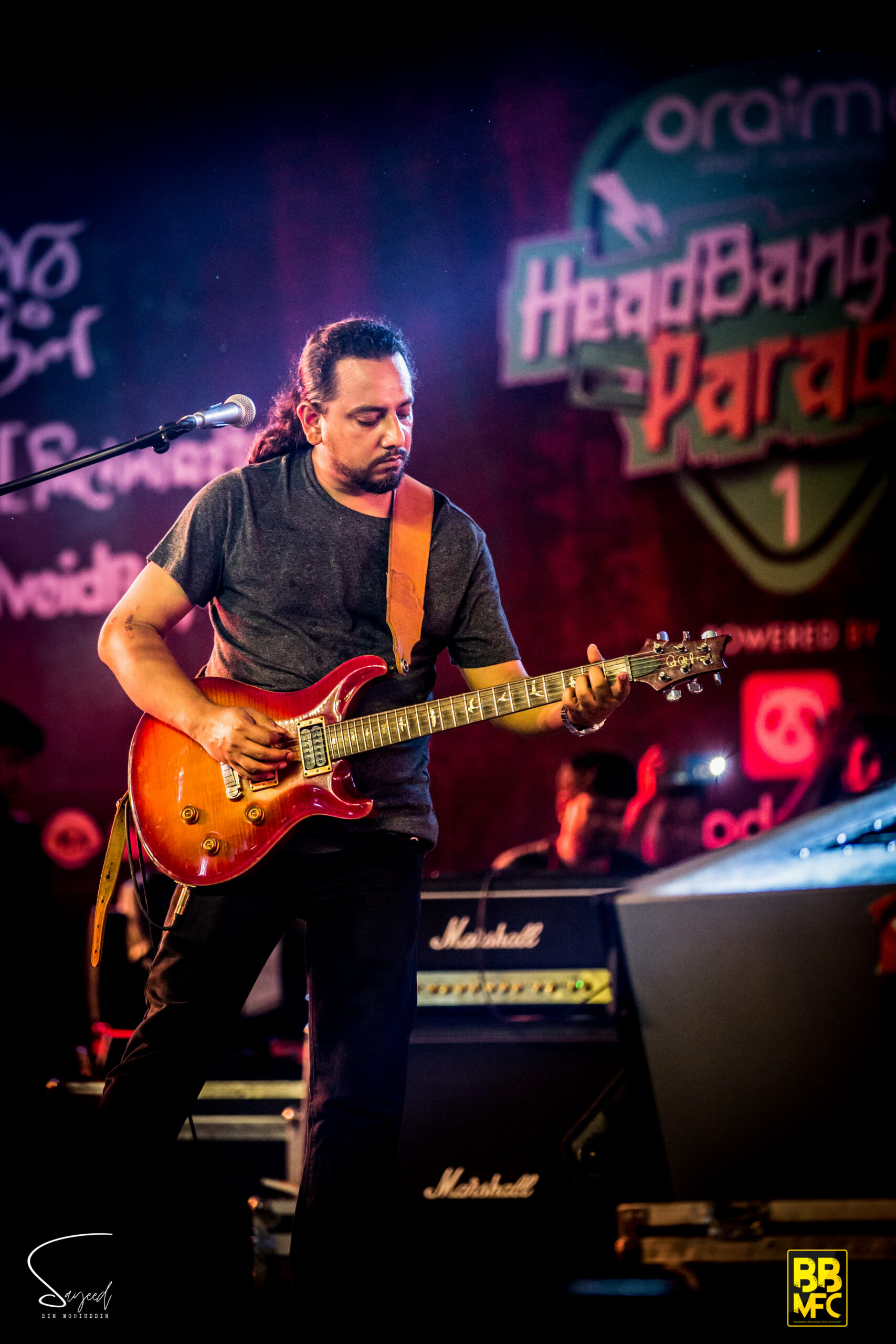 Guitarist focused on his playing in front of a "HeadBangers Parade" backdrop at a Dhaka concert — Sayeed BM