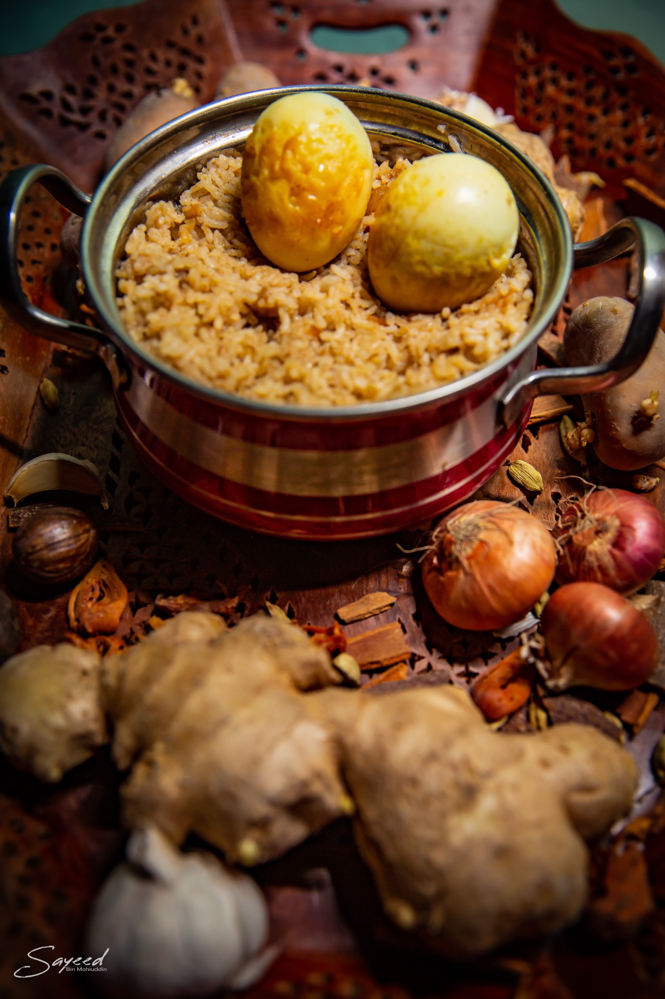 Pot of fragrant rice surrounded by whole spices, onions and ginger, overhead