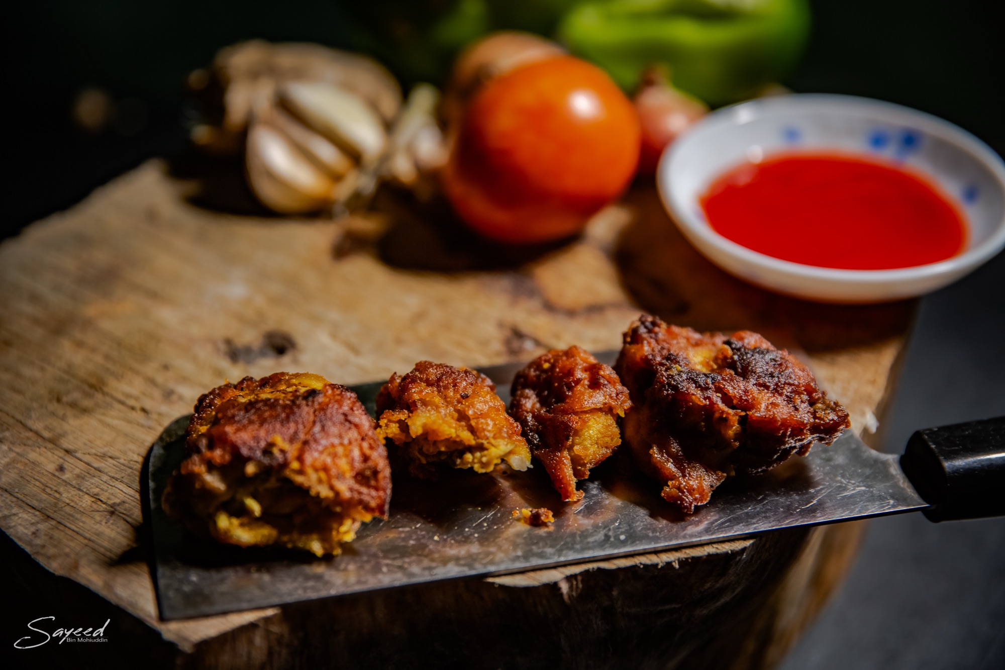 Overhead wooden board of grilled chicken tikka with tomatoes, garlic and dipping sauce