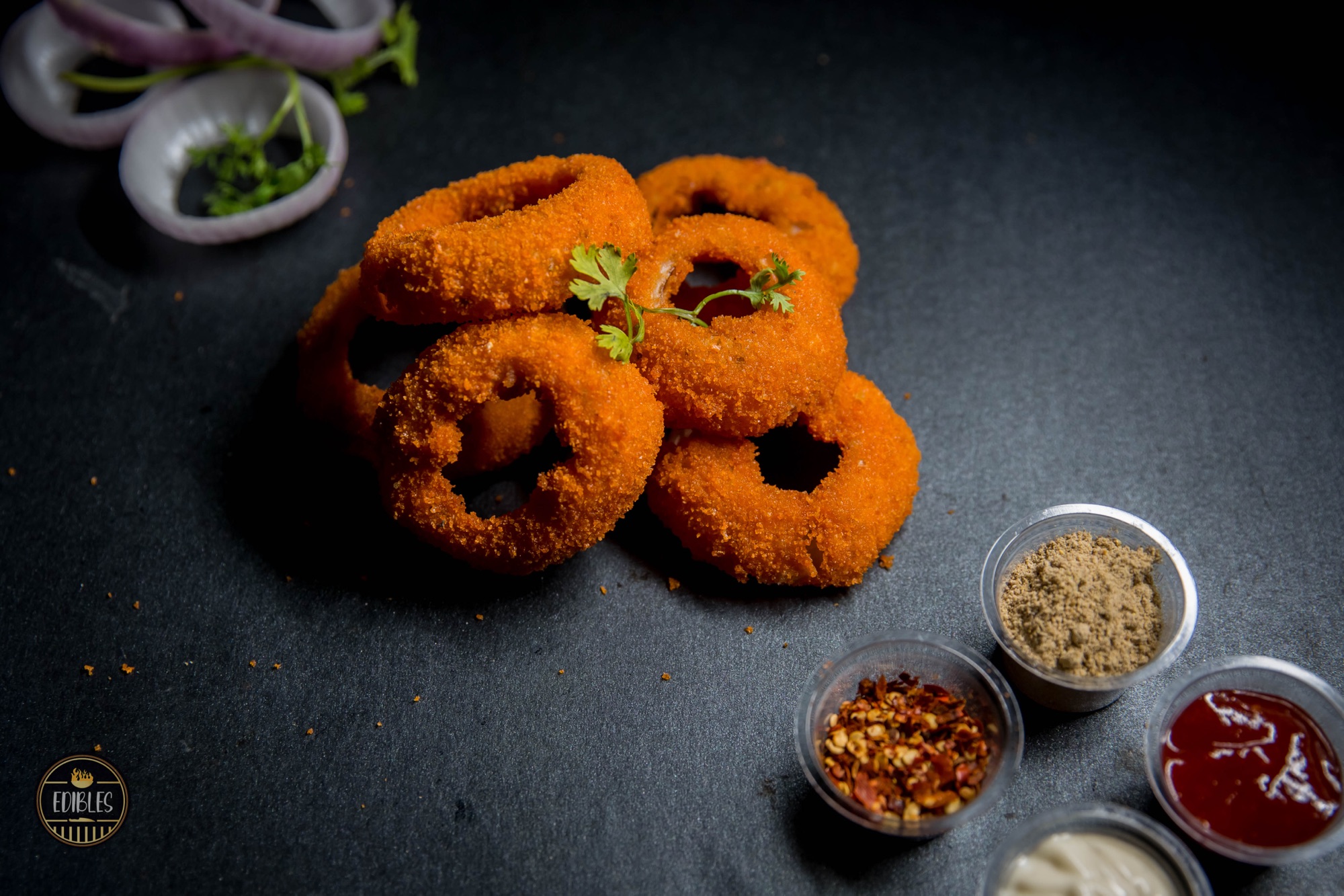 Stack of crispy onion rings with herb garnish and dipping sauce on a dark plate