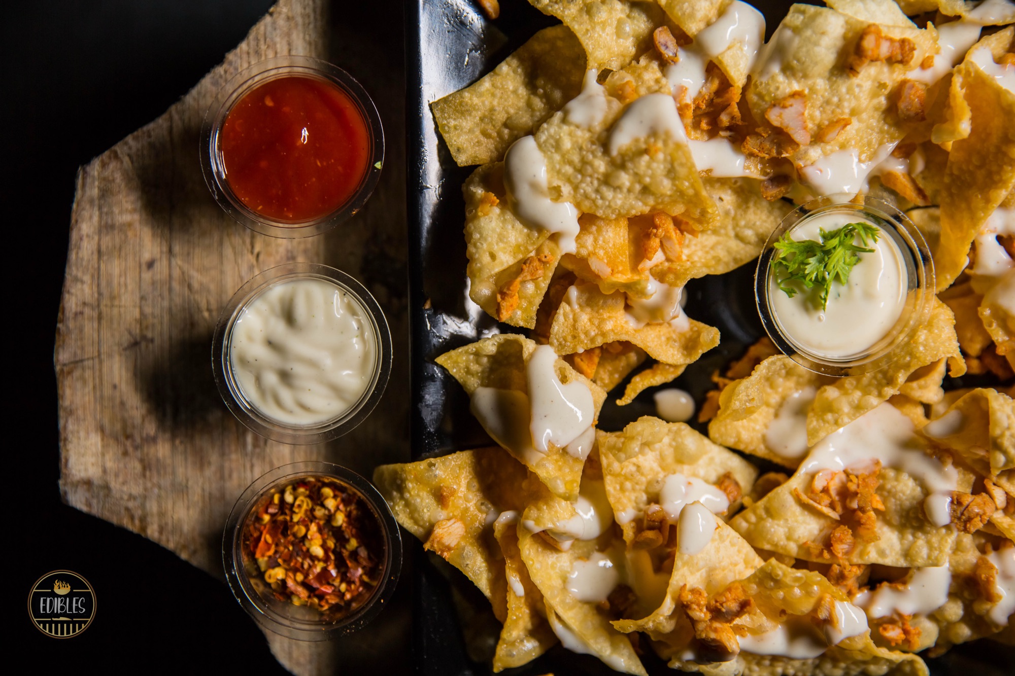 Overhead shot of crispy dumplings and chips with three dipping sauces on a wooden board