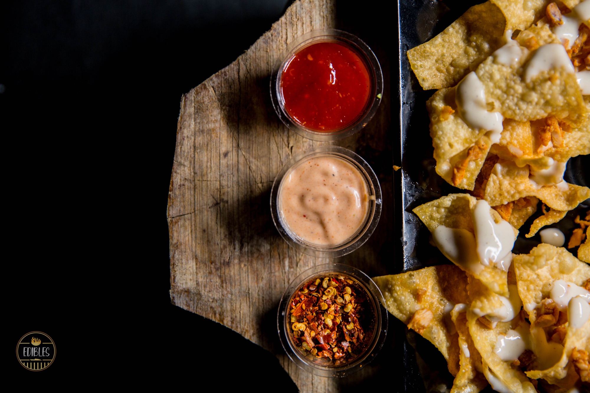 Overhead shot of a wooden board with nacho chips and three dipping sauces