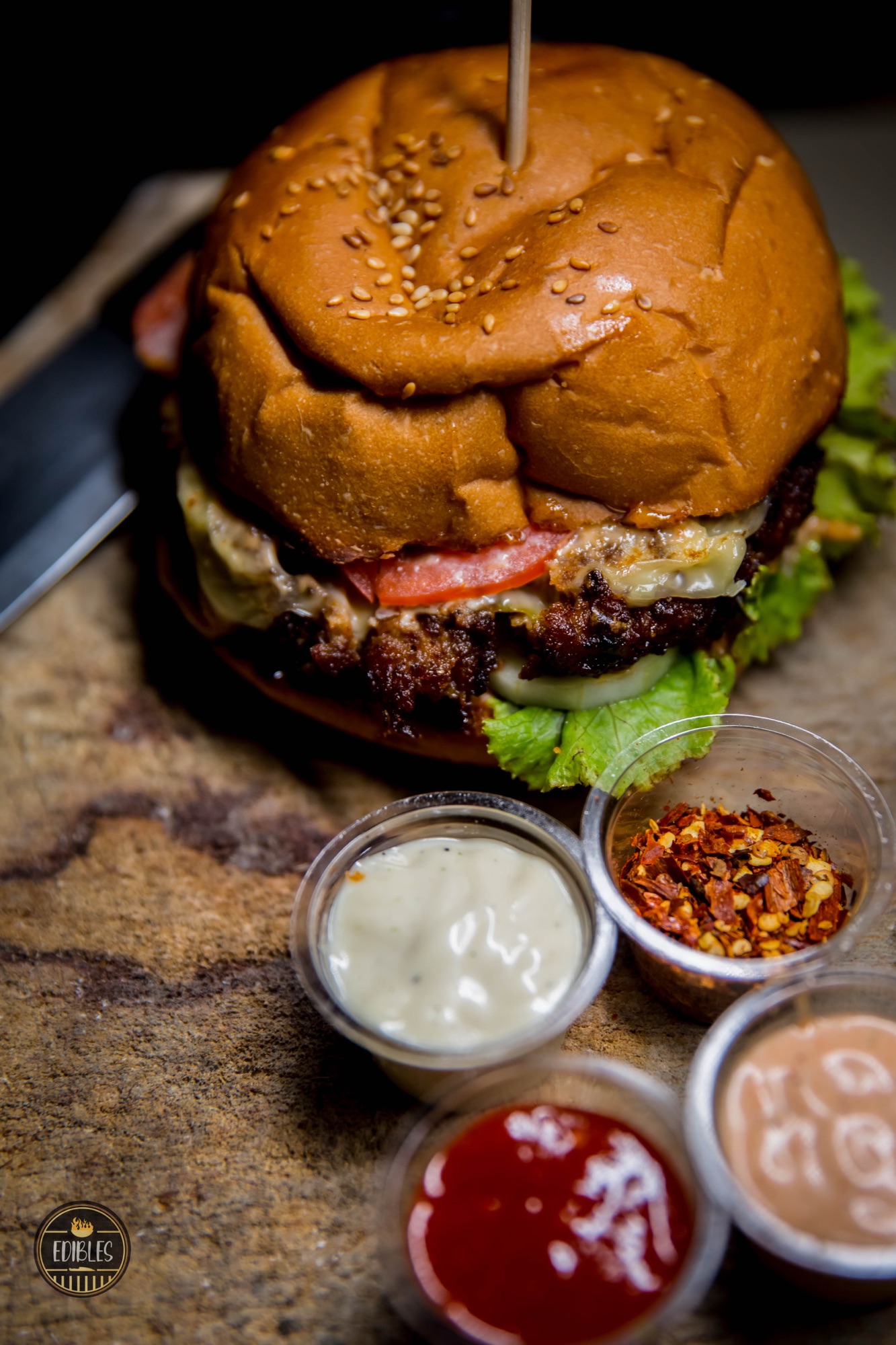 Close-up of a juicy burger with melted cheese, tomato and creamy dip on the side