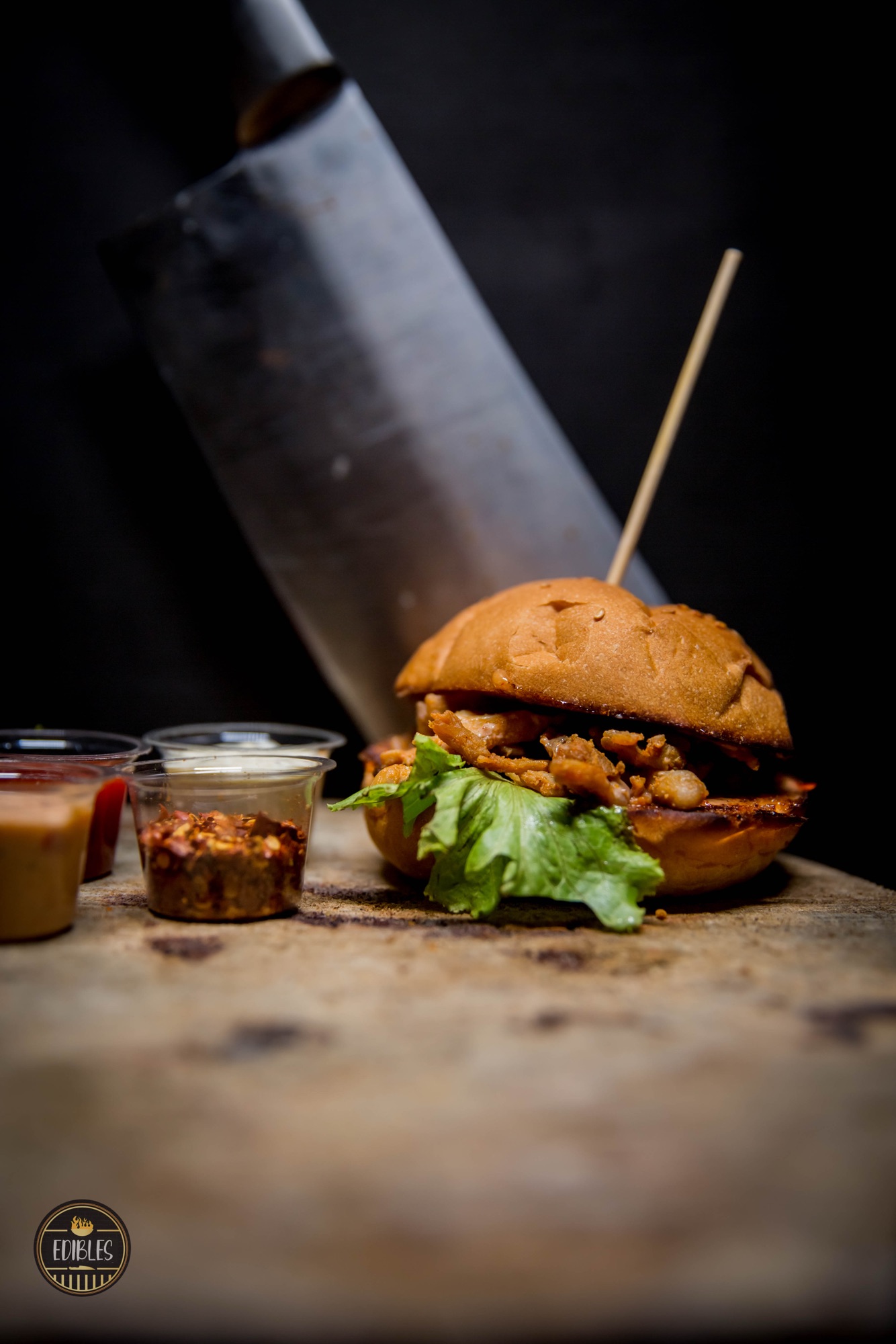 Stacked burger with crispy fries and dipping sauces on a rustic wooden board