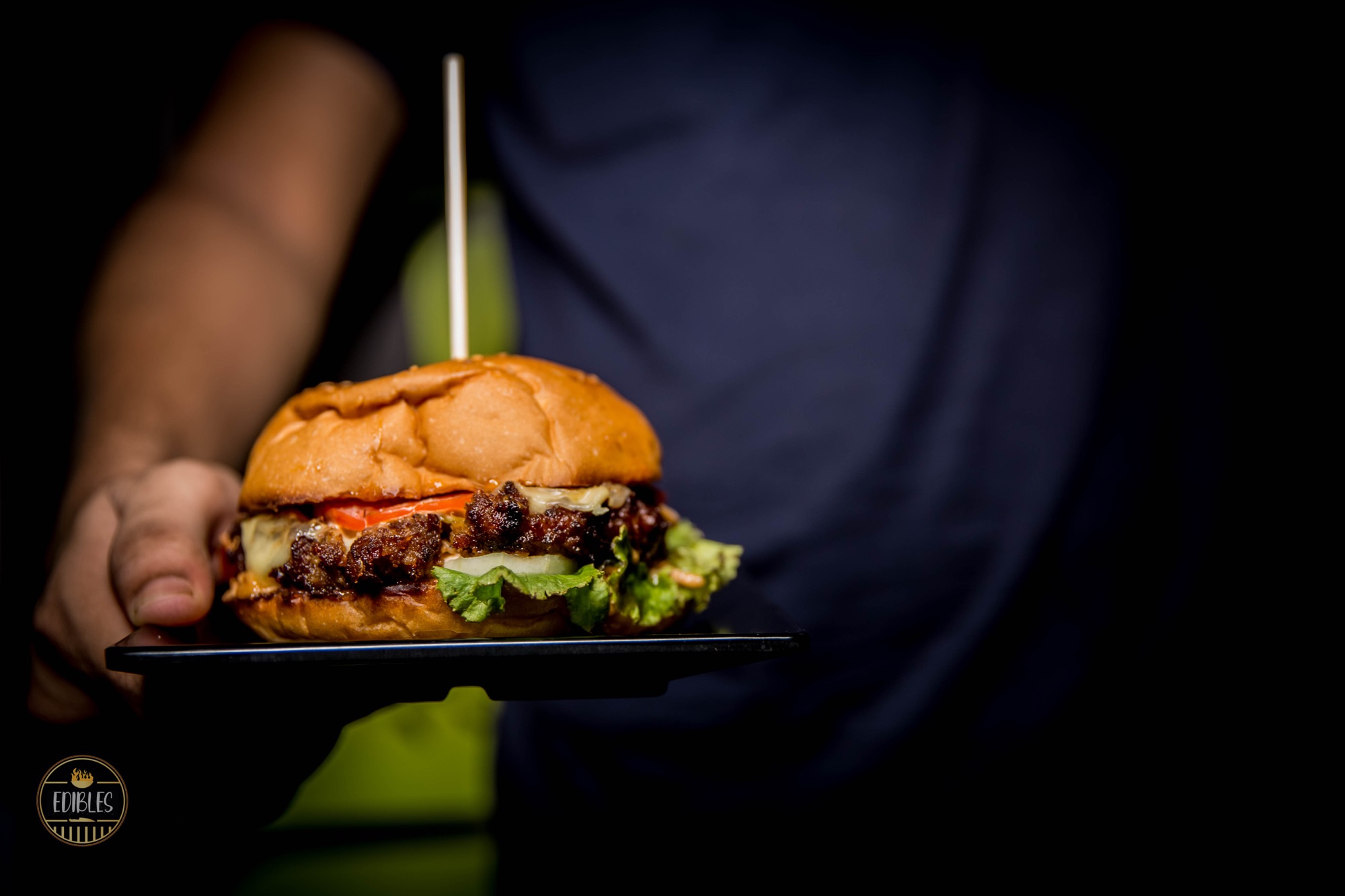 Close-up of a loaded burger with melted cheese and lettuce held on a tray