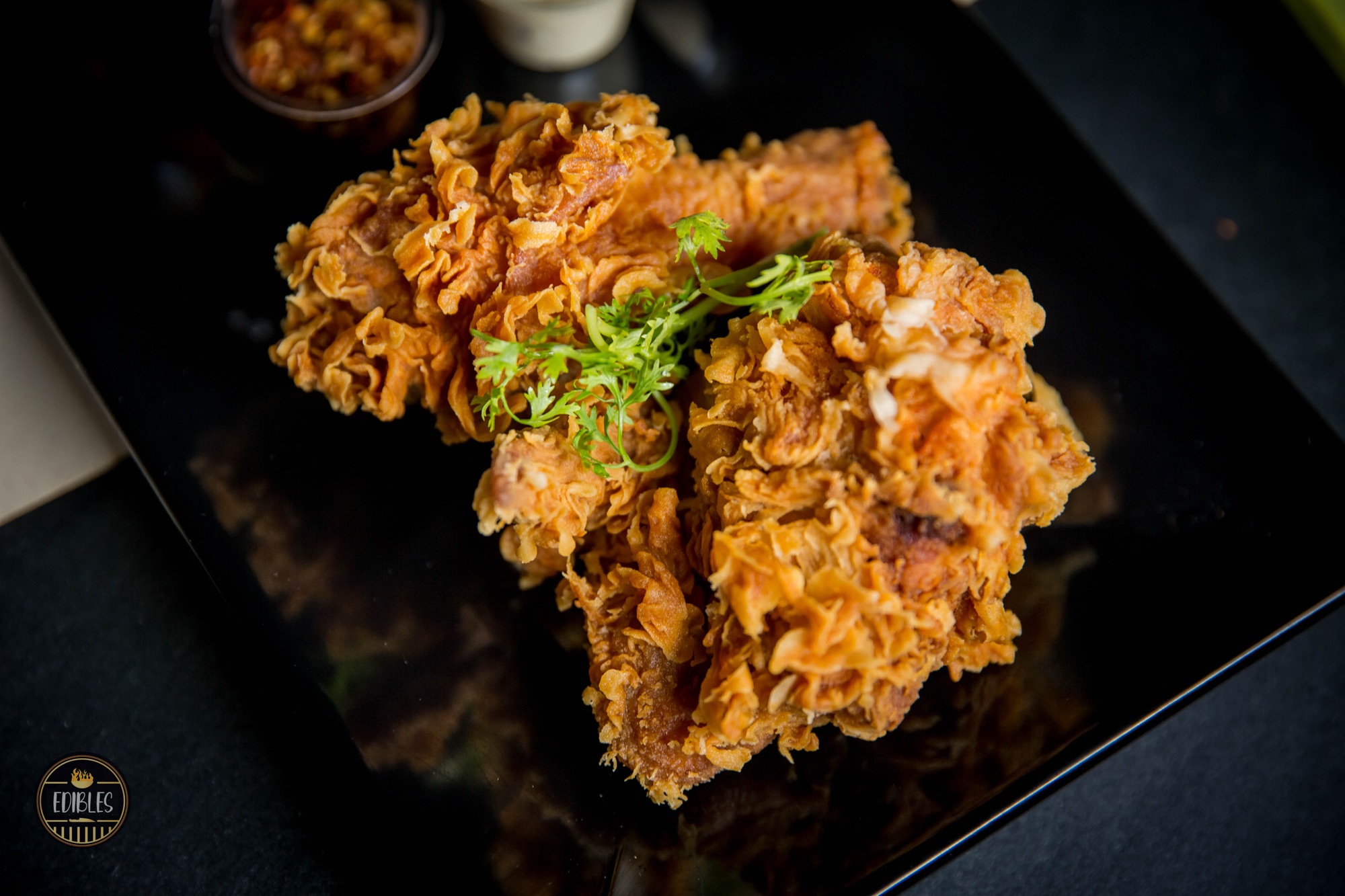 Crispy fried chicken piece garnished with fresh coriander on a dark plate