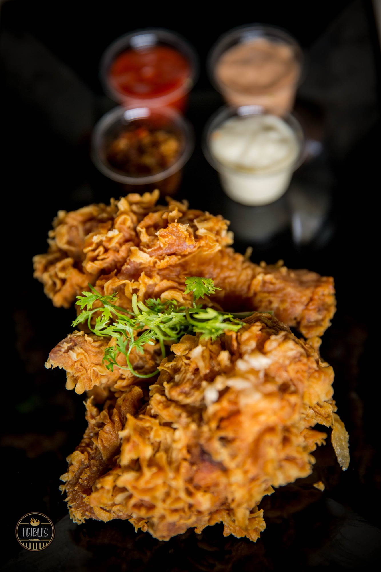 Pile of crispy fried chicken pieces with herb garnish on a dark background