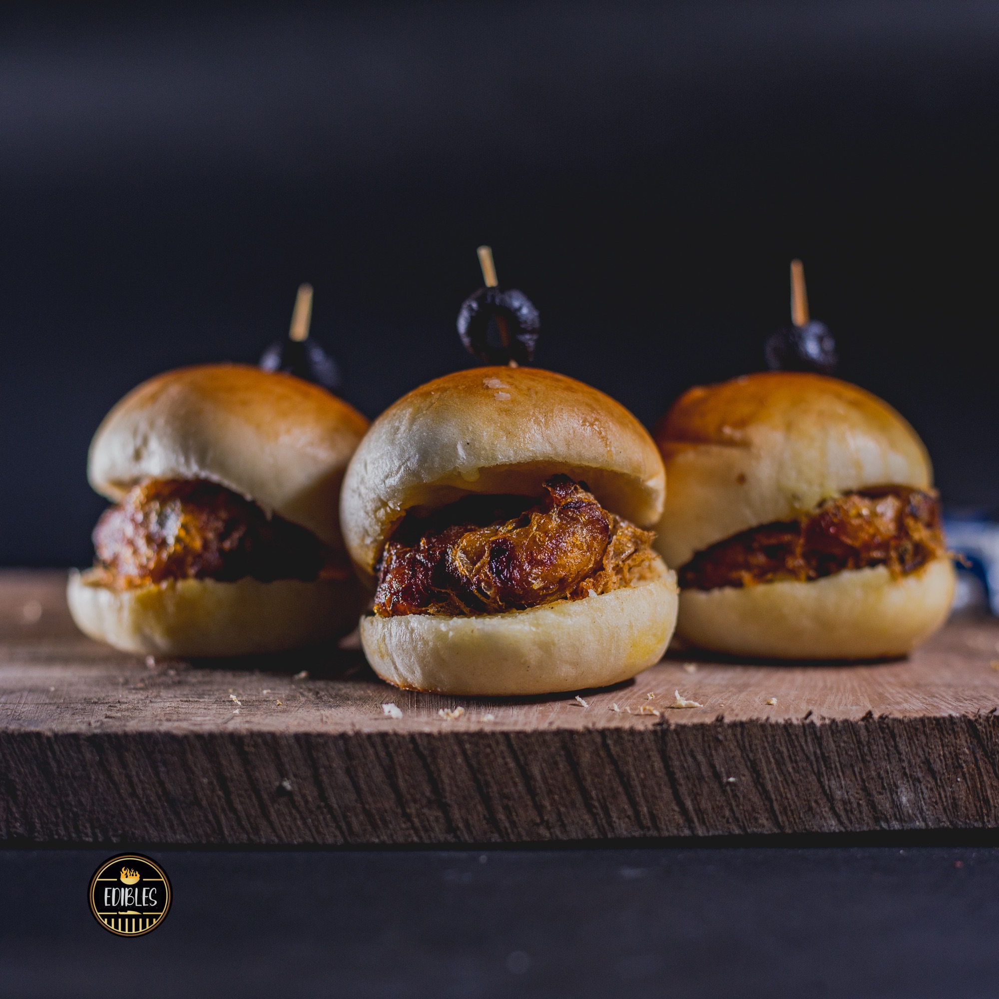 Three mini beef sliders lined up on a dark wooden board