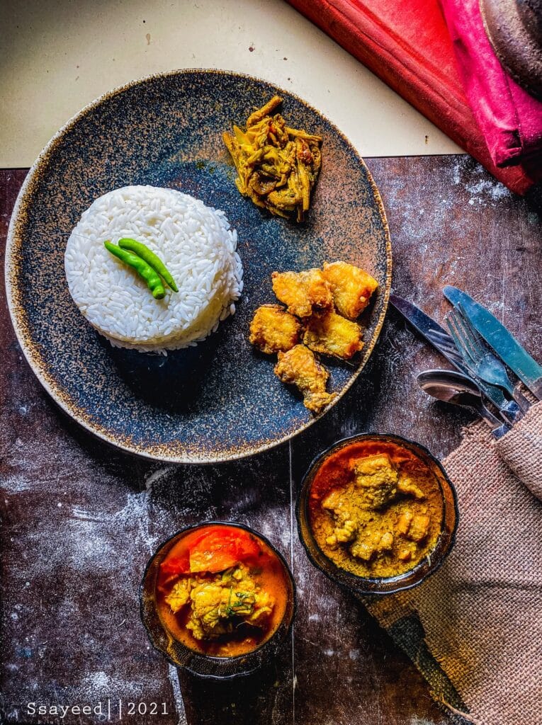 Overhead flat lay of a full Bengali meal with rice, bhorta, and fried fish