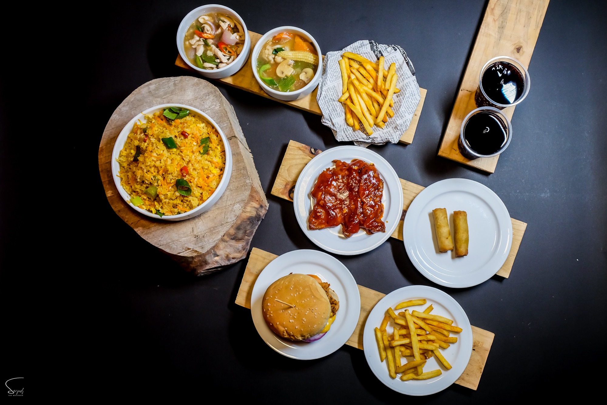 Overhead flat lay of a fast-food spread with burgers, fries, fried rolls and dipping sauces