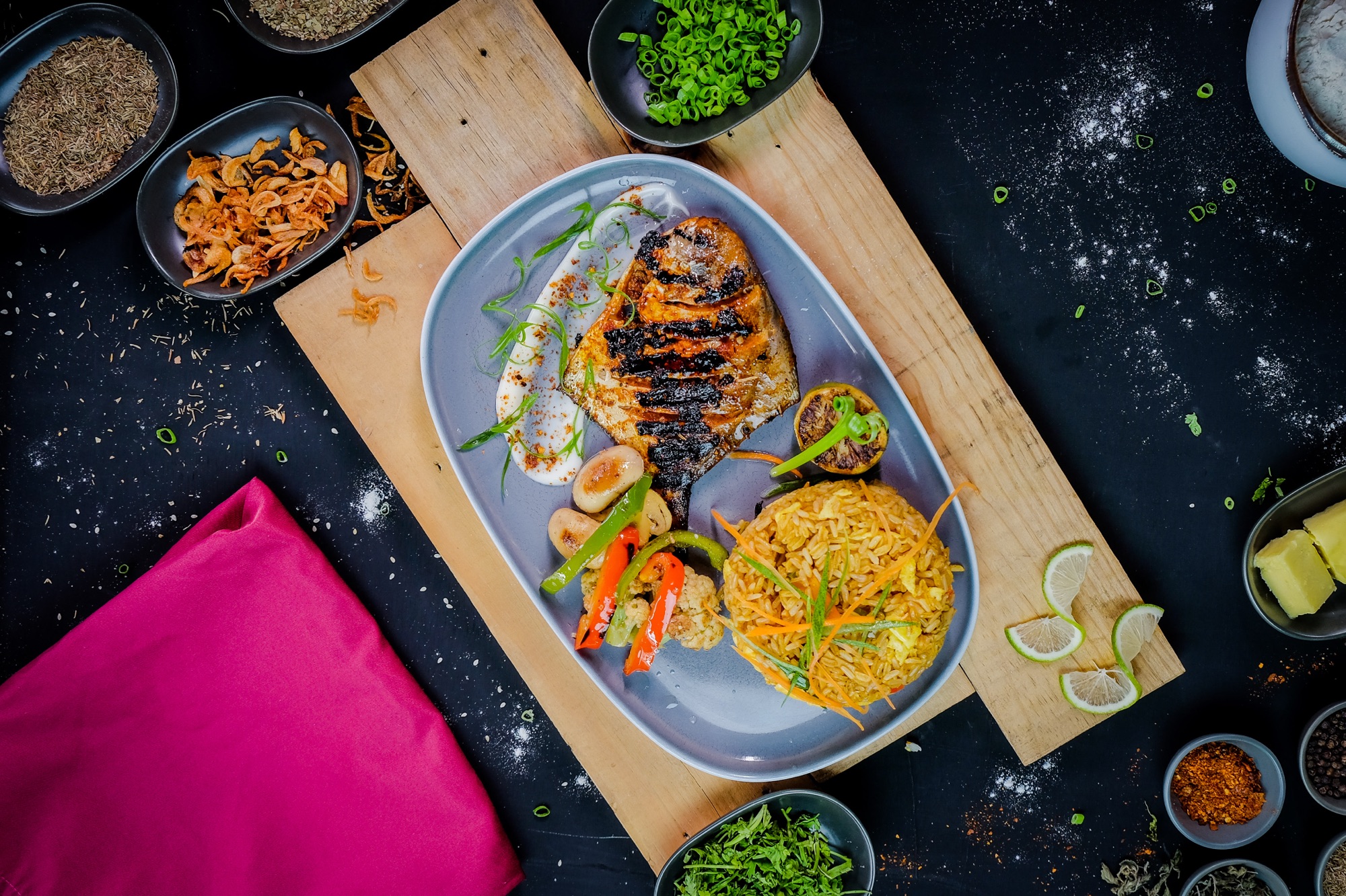 Overhead shot of grilled fish, rice ball and salad plated on a grey ceramic dish with a pink napkin