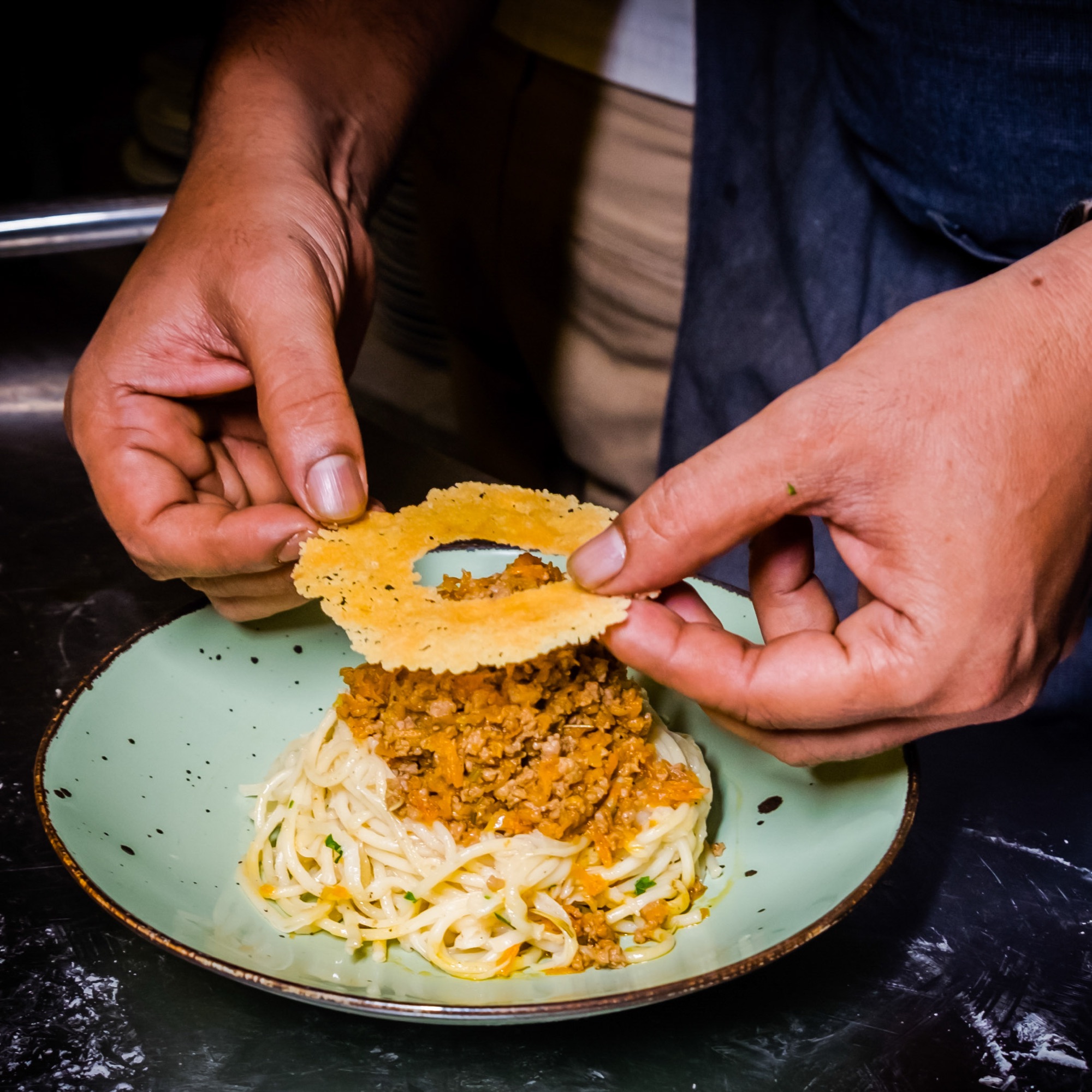 Chef's hands placing fresh basil leaves on a plated pasta dish