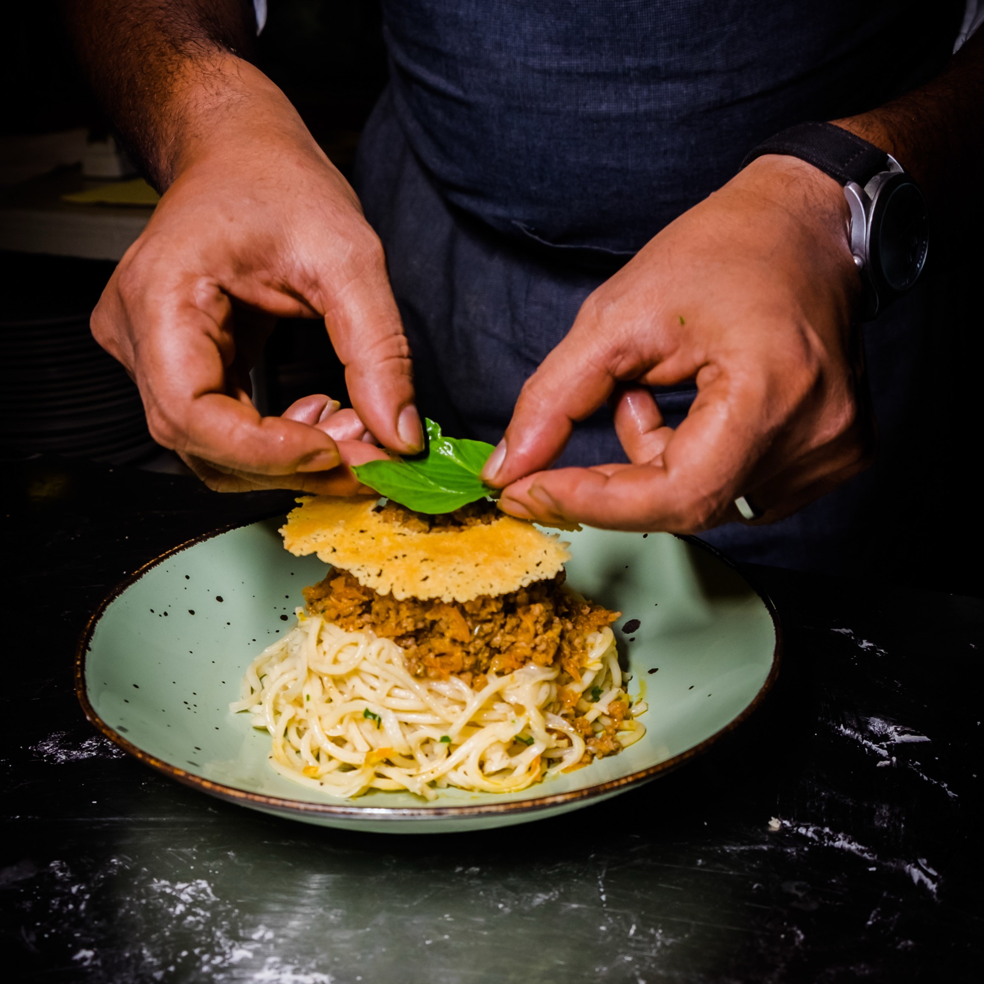Close-up of hands garnishing a pasta dish with fresh basil before serving — Sayeed BM