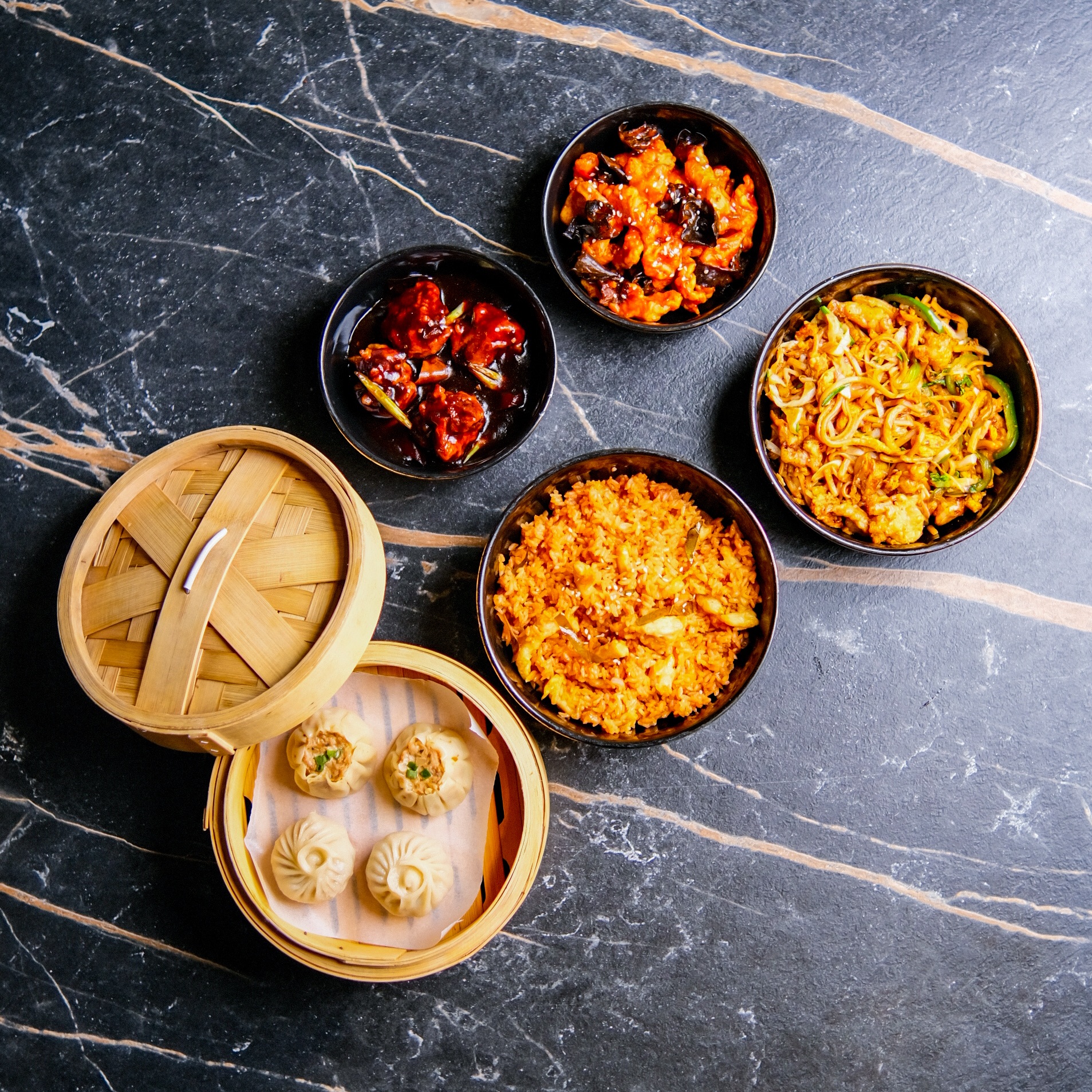 Overhead spread of bamboo dim sum steamers and fried rice bowls on a marble table