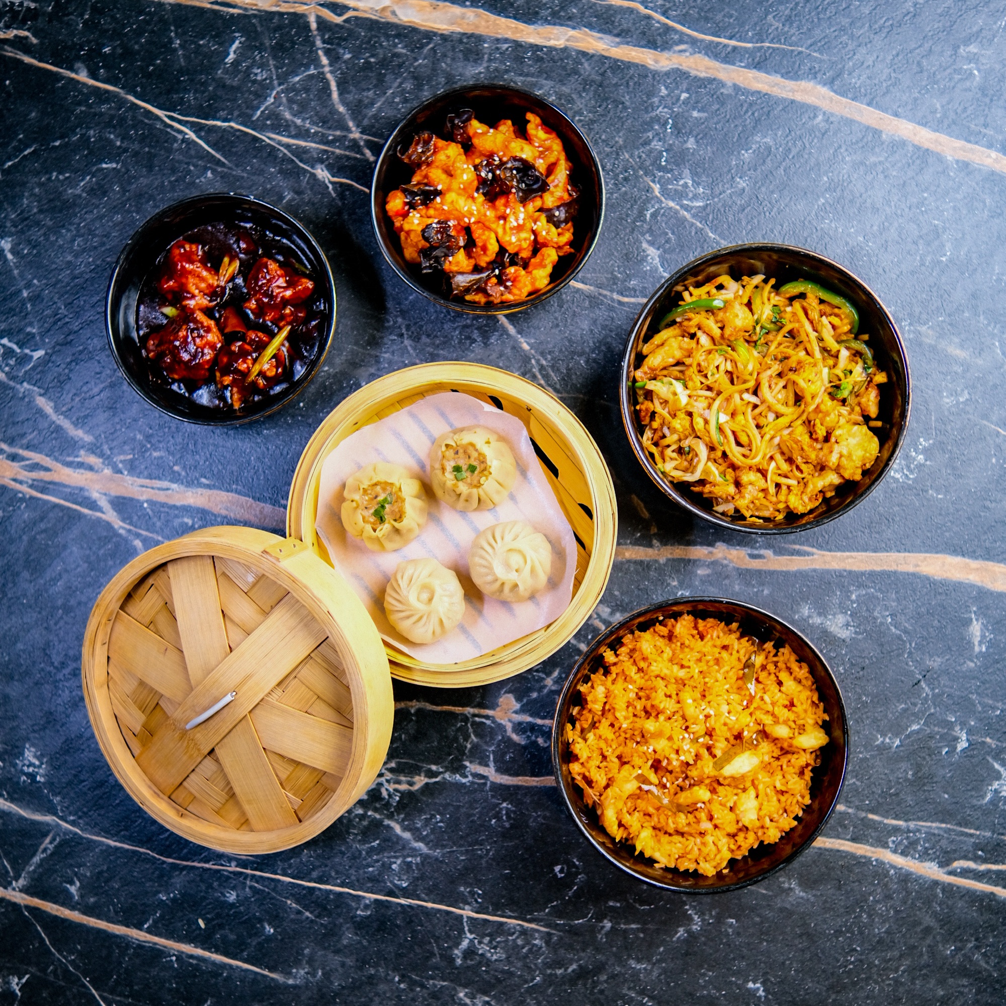 Overhead bowls of dumplings and fried rice on dark marble