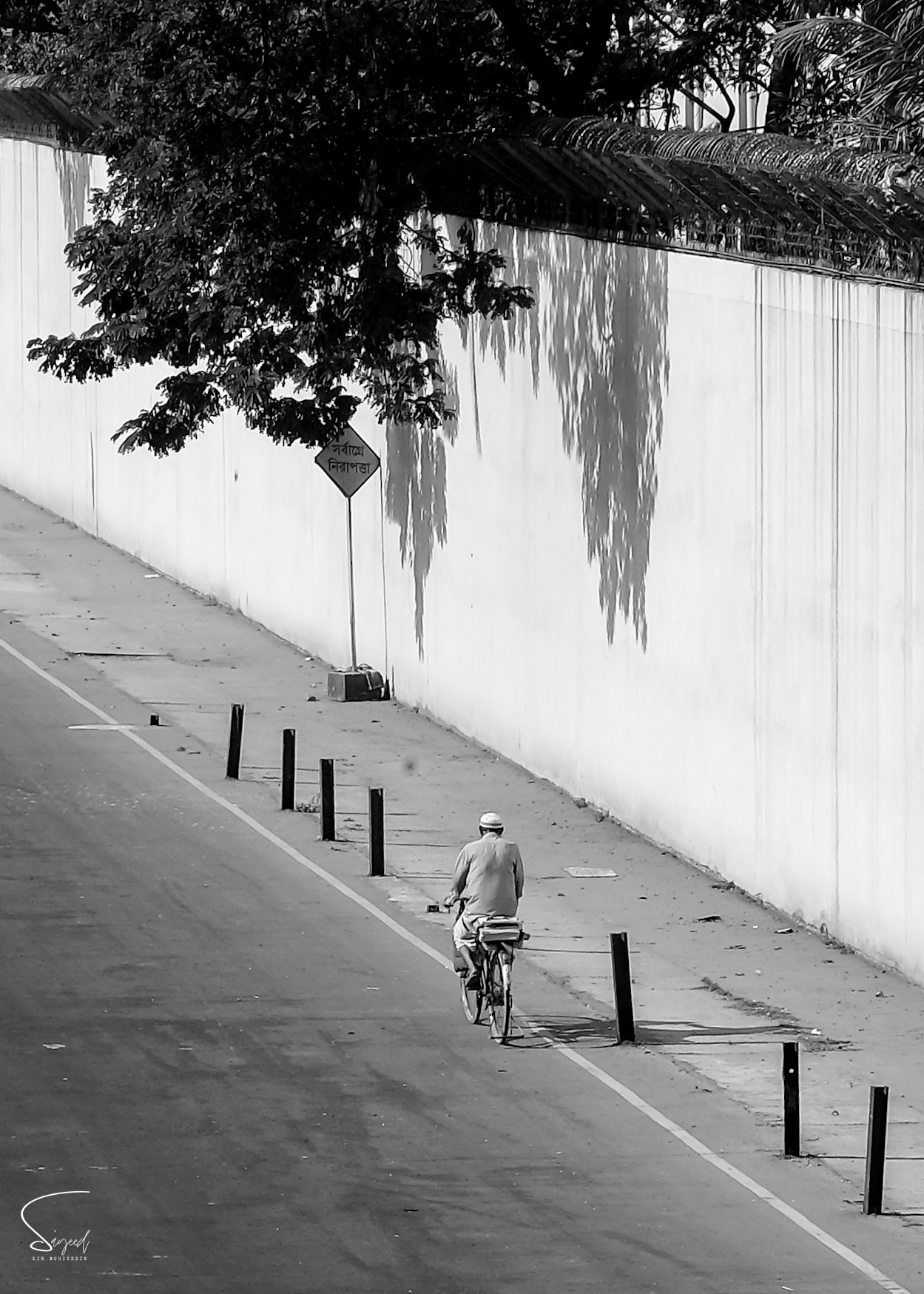 A lone cyclist on a wide empty urban road, black and white, Dhaka