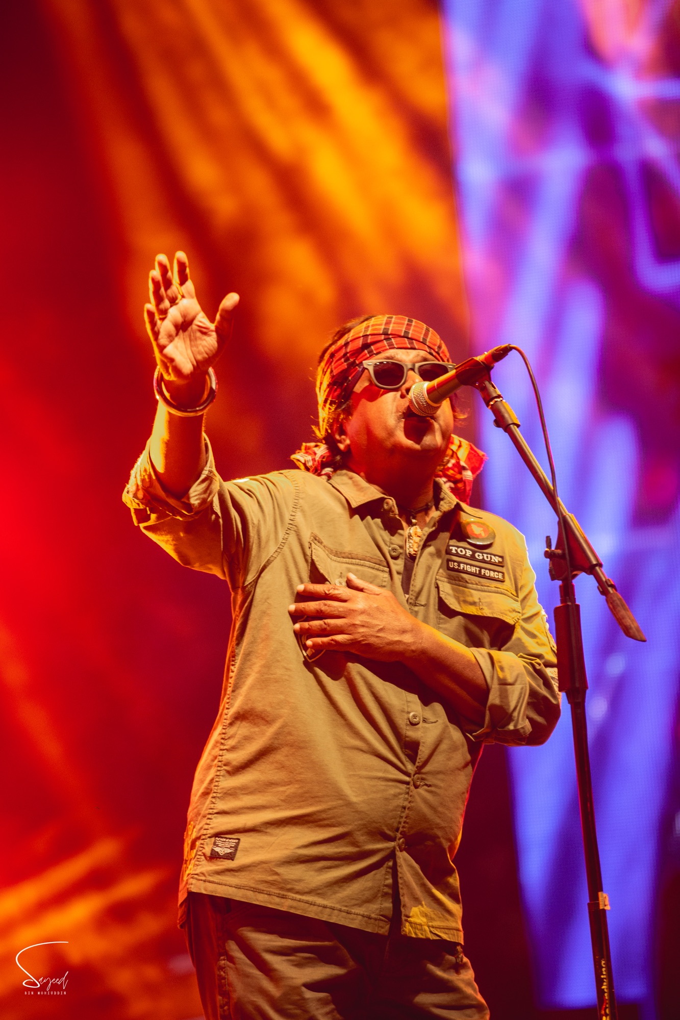 Singer in a bandana and sunglasses performing under orange and purple light at a live concert in Dhaka — Sayeed BM