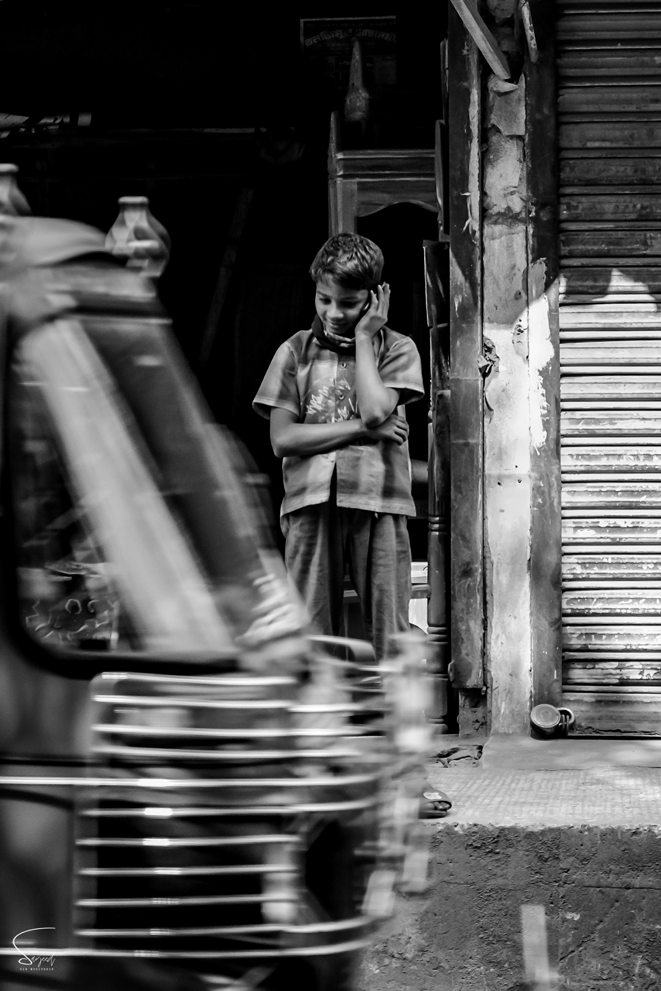 A child seated in a doorway, light falling across the face, black and white, Chittagong