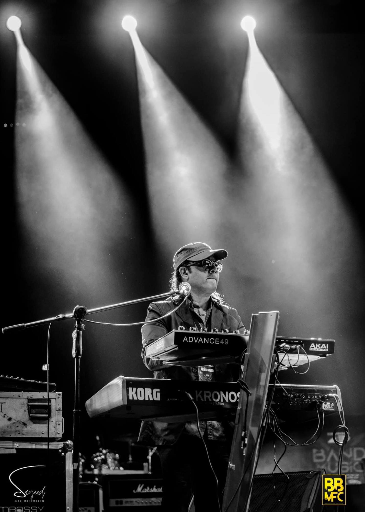 Keyboardist performing under dramatic spotlight rays, black-and-white, vertical shot from a Shironamhin concert in Dhaka — Sayeed BM