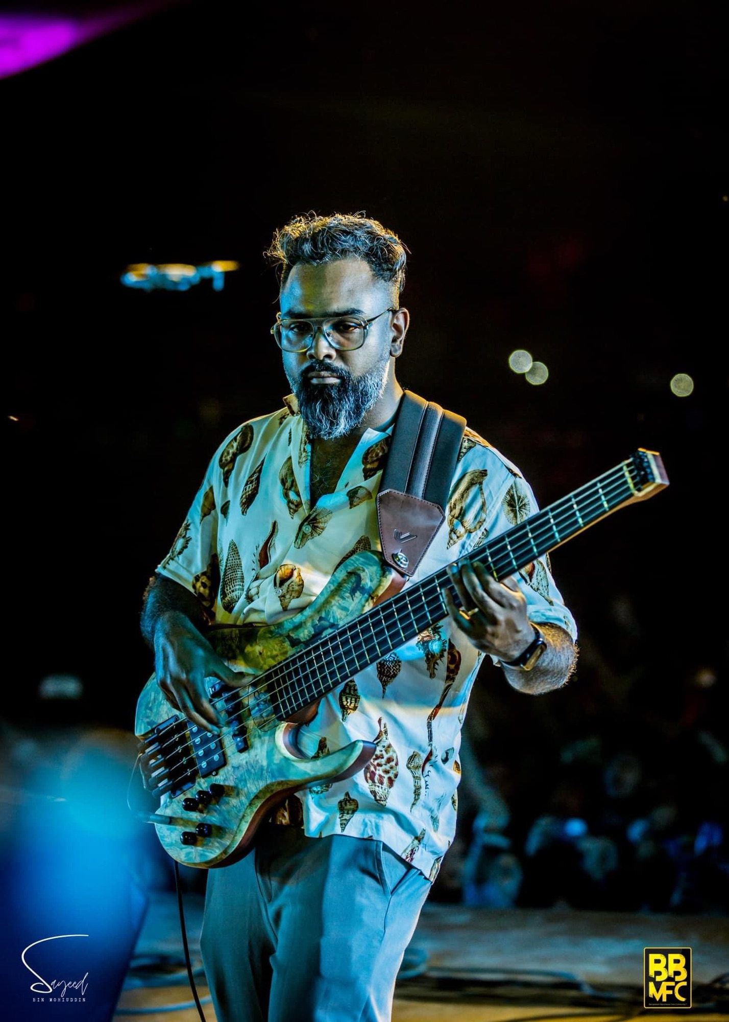 Bassist in a leaf-print shirt performing under blue stage light at a Shironamhin concert in Dhaka — Sayeed BM