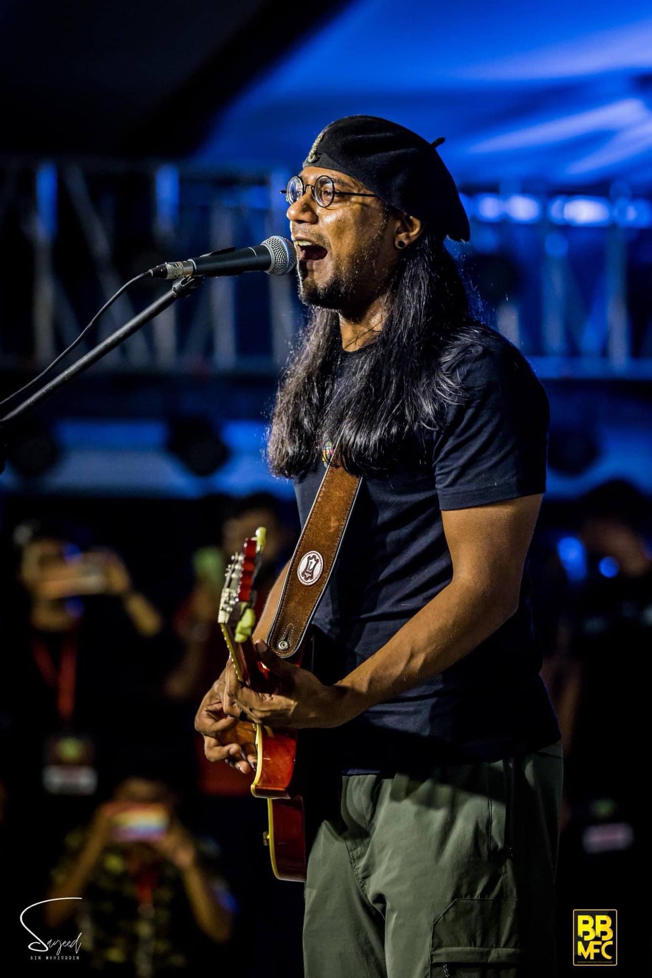 Long-haired singer performing under blue stage light with the crowd visible below, Shironamhin concert in Dhaka — Sayeed BM