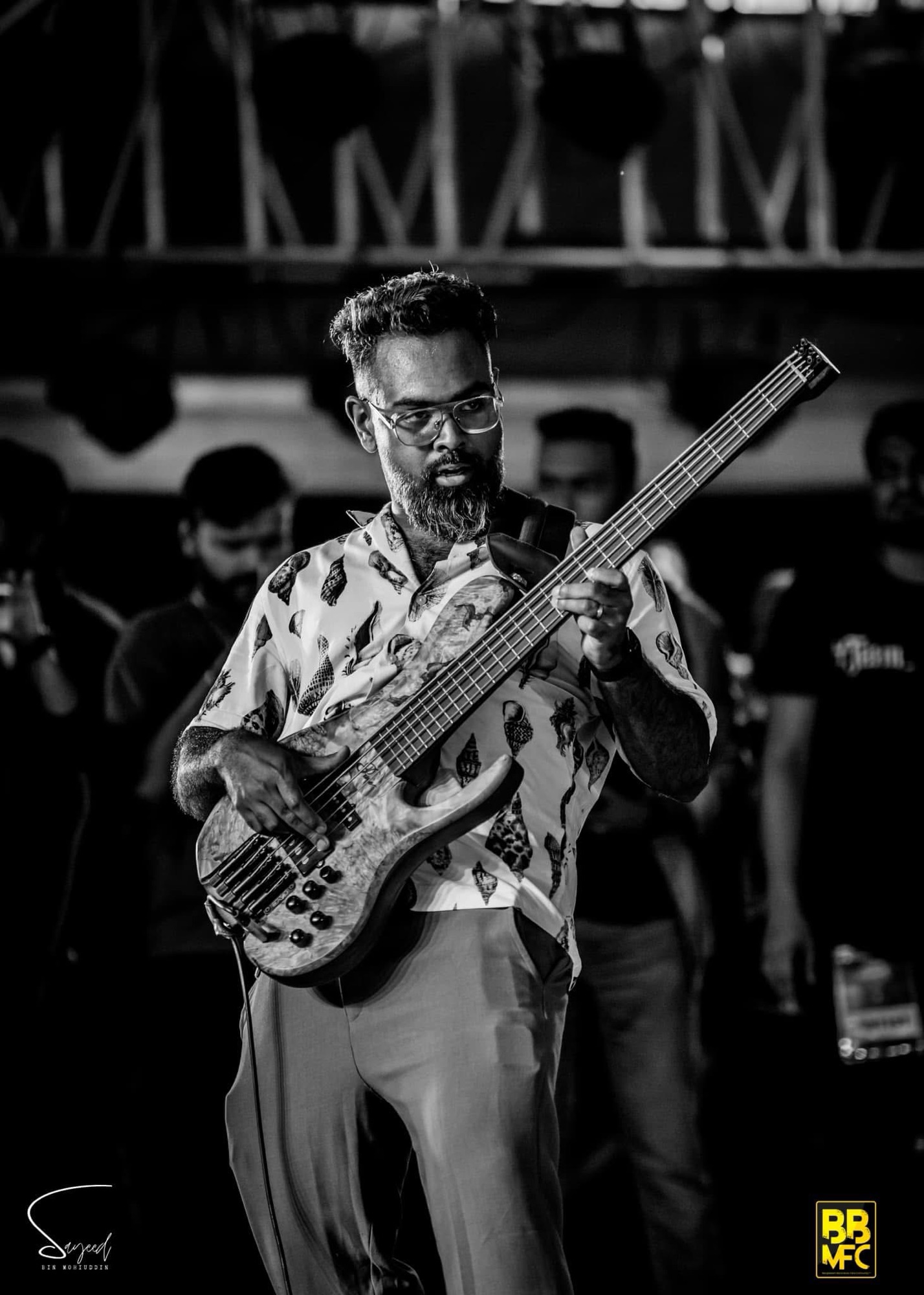 Bassist in a leaf-print shirt with the crowd visible behind, black-and-white, Shironamhin concert in Dhaka — Sayeed BM
