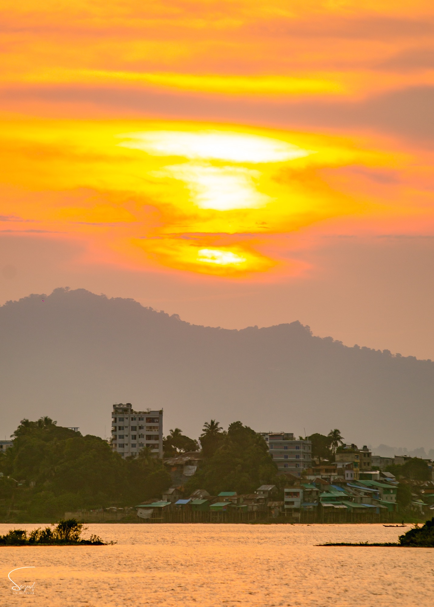 A motorcyclist on an elevated flyover under an orange sunset sky, Chattogram