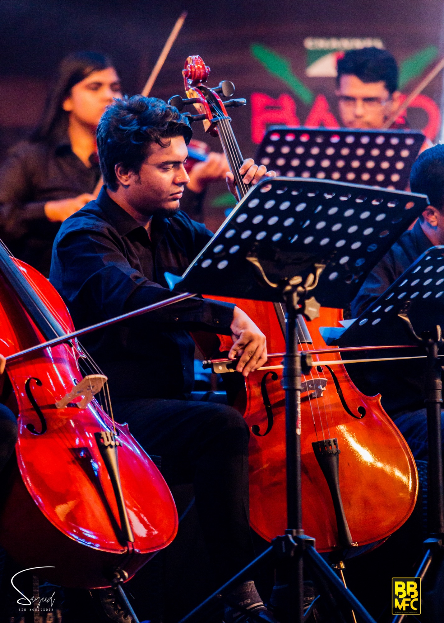 Cellist playing among a string section on stage at a live concert in Dhaka — Sayeed BM