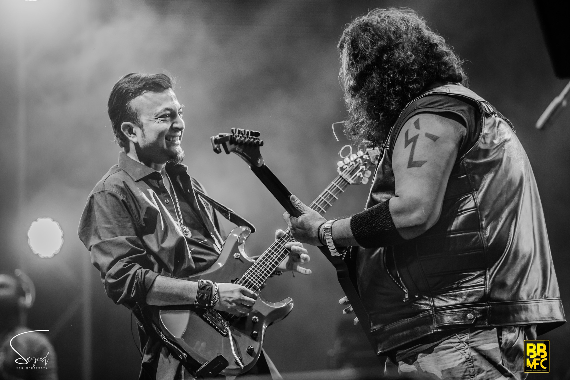 Two guitarists facing each other and smiling mid-song, black-and-white shot from a live concert in Dhaka — Sayeed BM