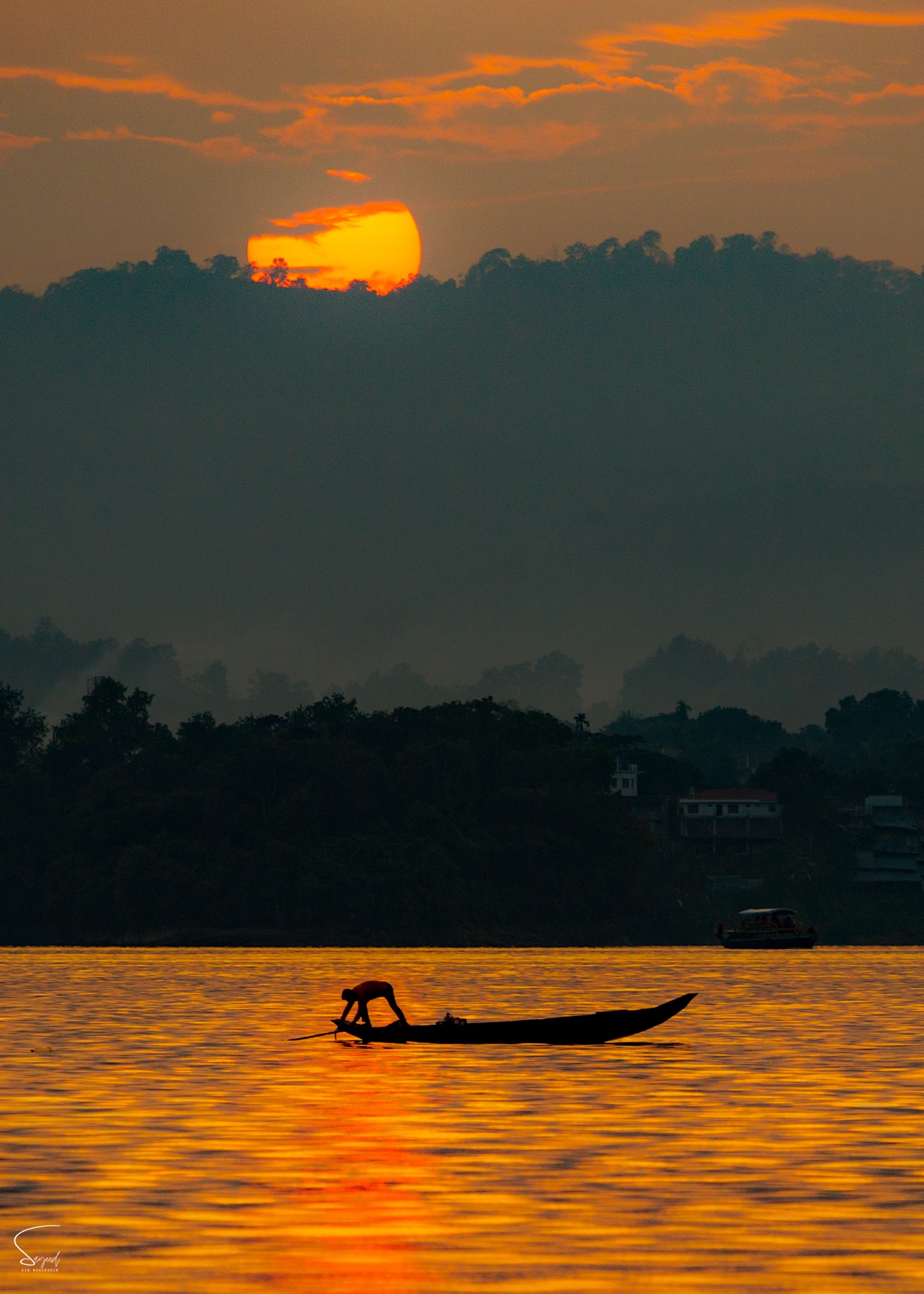 A fisherman in a traditional wooden boat at sunset with mountains behind, Rangamati