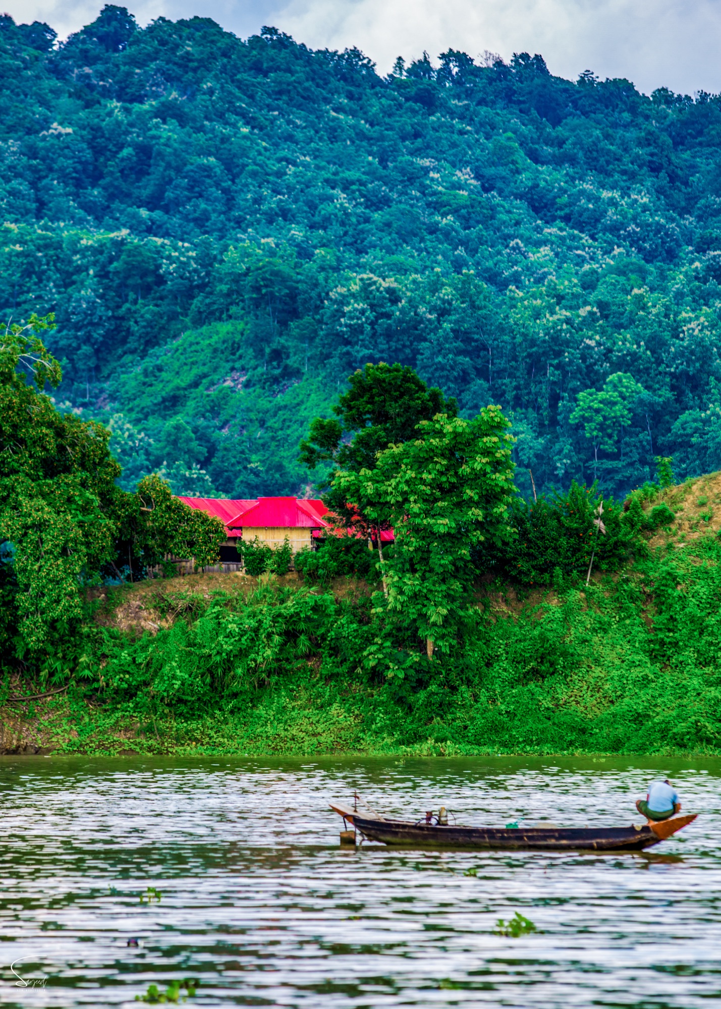 A fisherman on the water below the big mountains of Rangamati