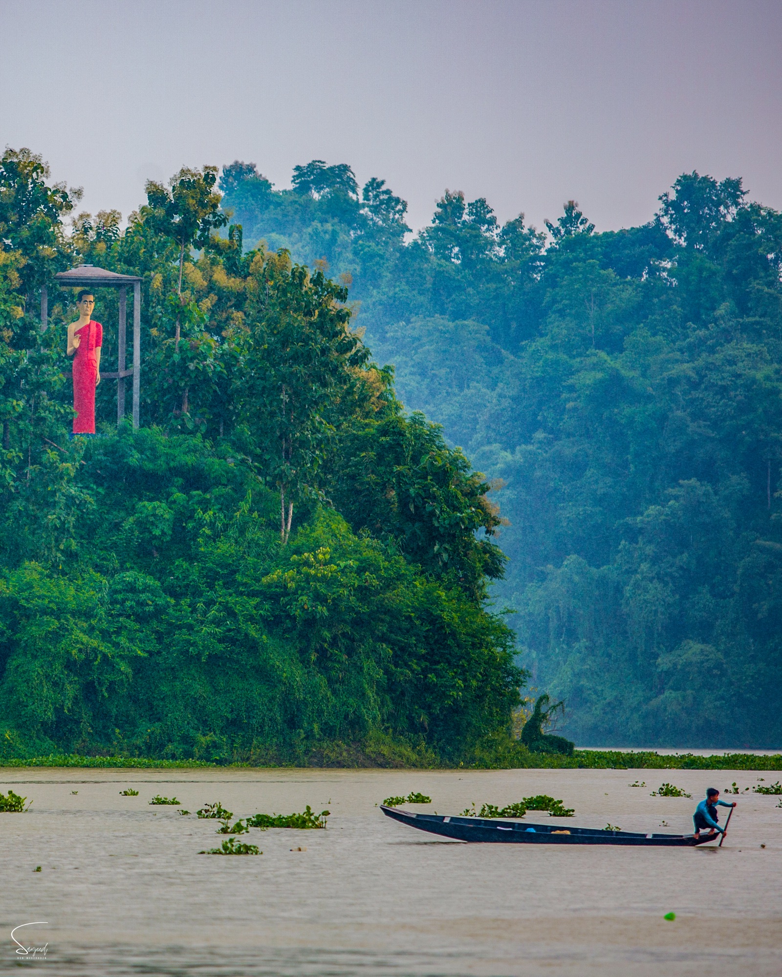 A wooden fishing boat with a Buddhist statue in the background on a rainy day, Rangamati