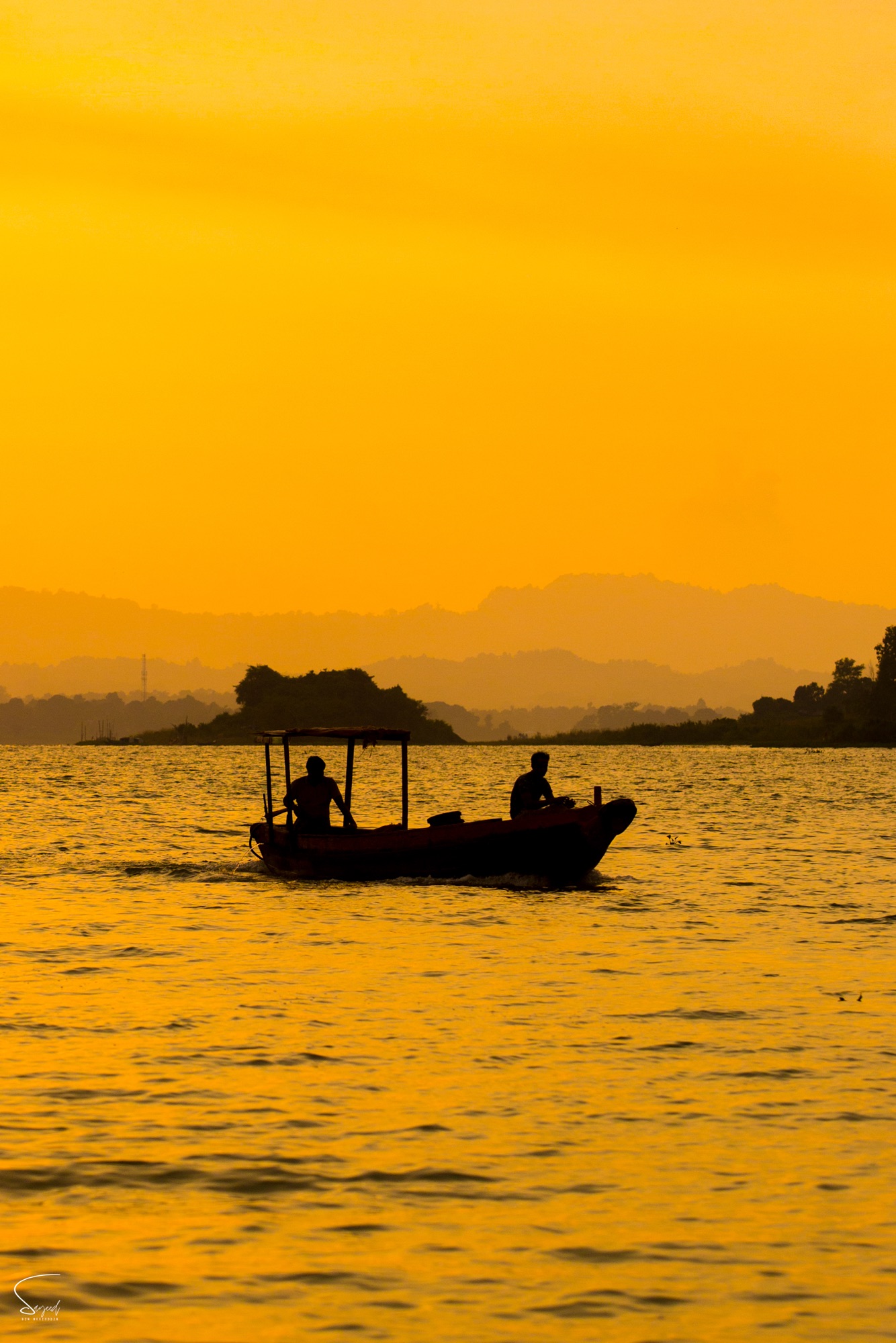 Silhouette of a wooden boat with two fishermen at golden hour, Rangamati