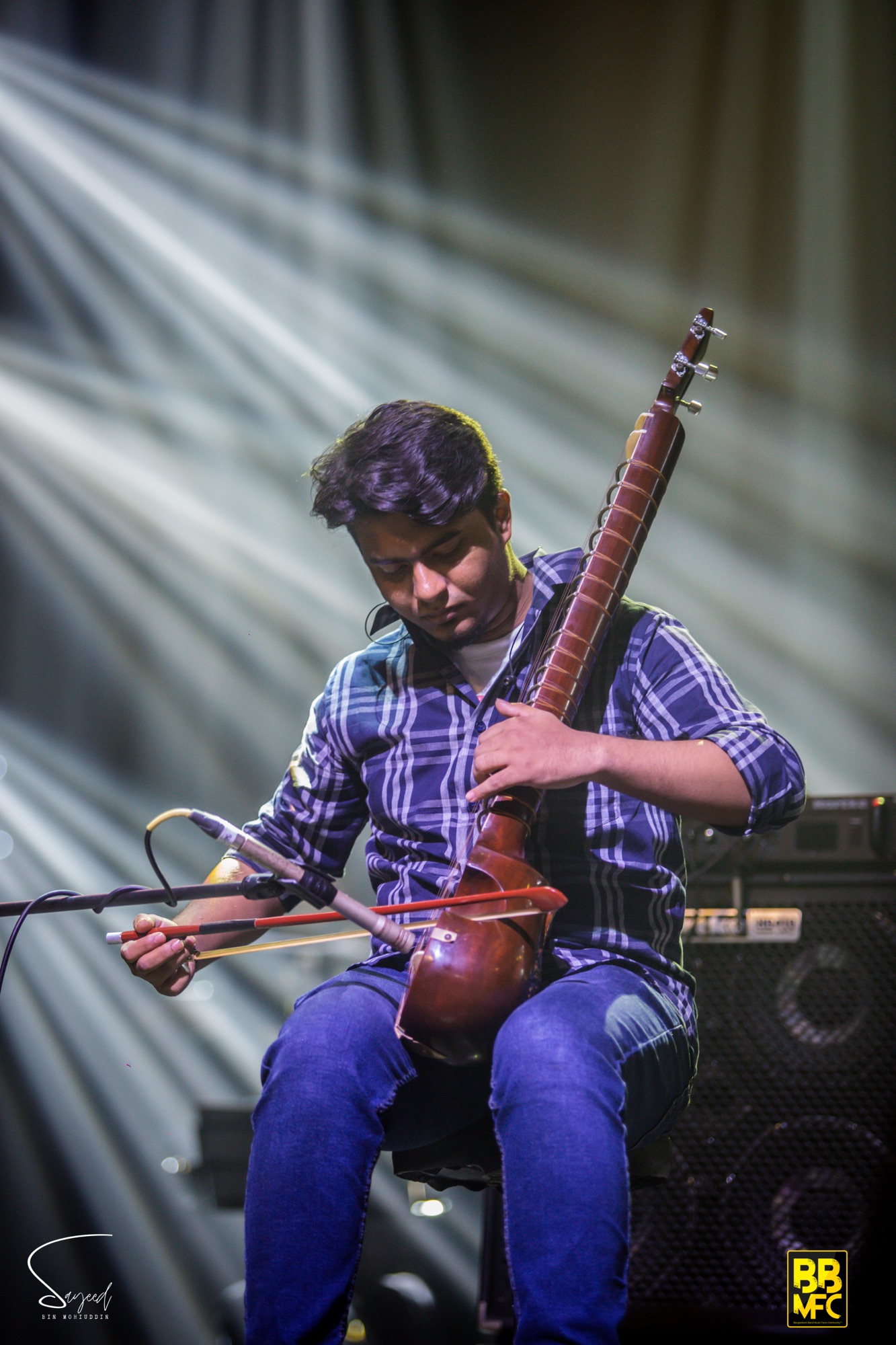 Musician playing a sarod, a traditional string instrument, under purple stage light at a Shironamhin concert in Dhaka — Sayeed BM